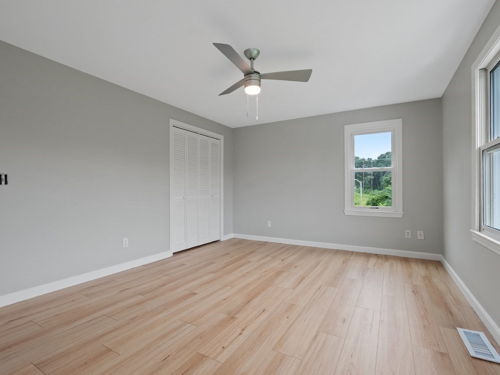 Empty bedroom with gray walls, light plank flooring, white closet doors, and a ceiling fan.