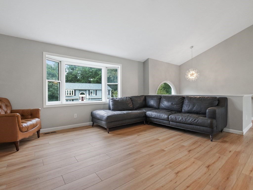 Living room with a dark sectional, brown leather armchair, wood floors, and a wide window.