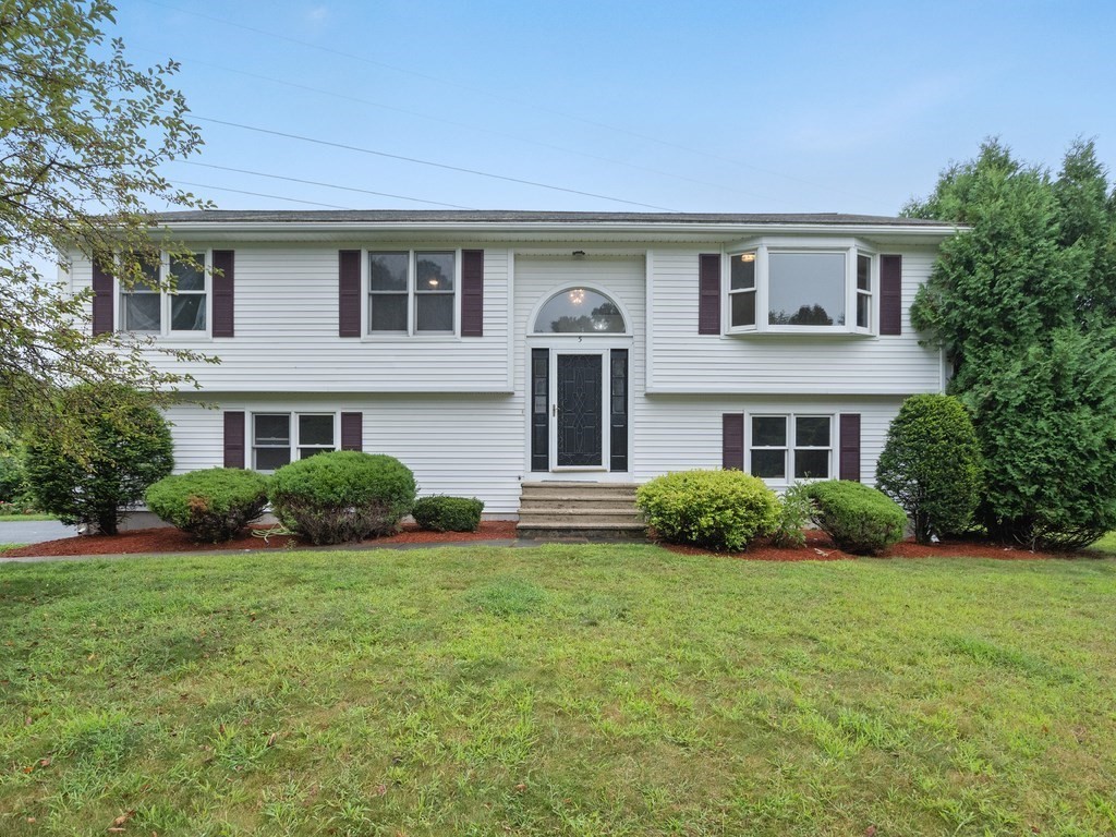 White split-level house with dark shutters, a projecting bay window, and shrubs along the front.