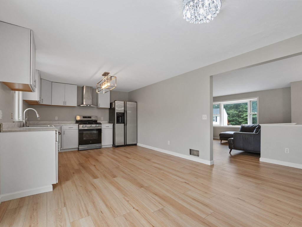 Open-plan kitchen with stainless steel appliances and wood floors, adjoining a living area with a dark sofa.