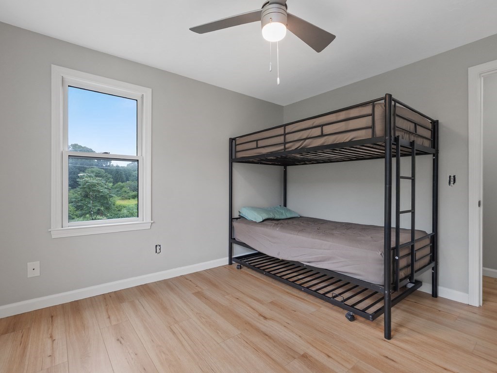 Bedroom with a black metal bunk bed, light wood flooring, and a window overlooking trees.