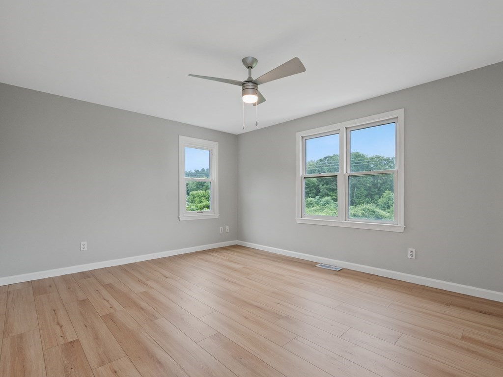 Vacant bedroom with light wood floors, gray walls, two windows, and a ceiling fan.