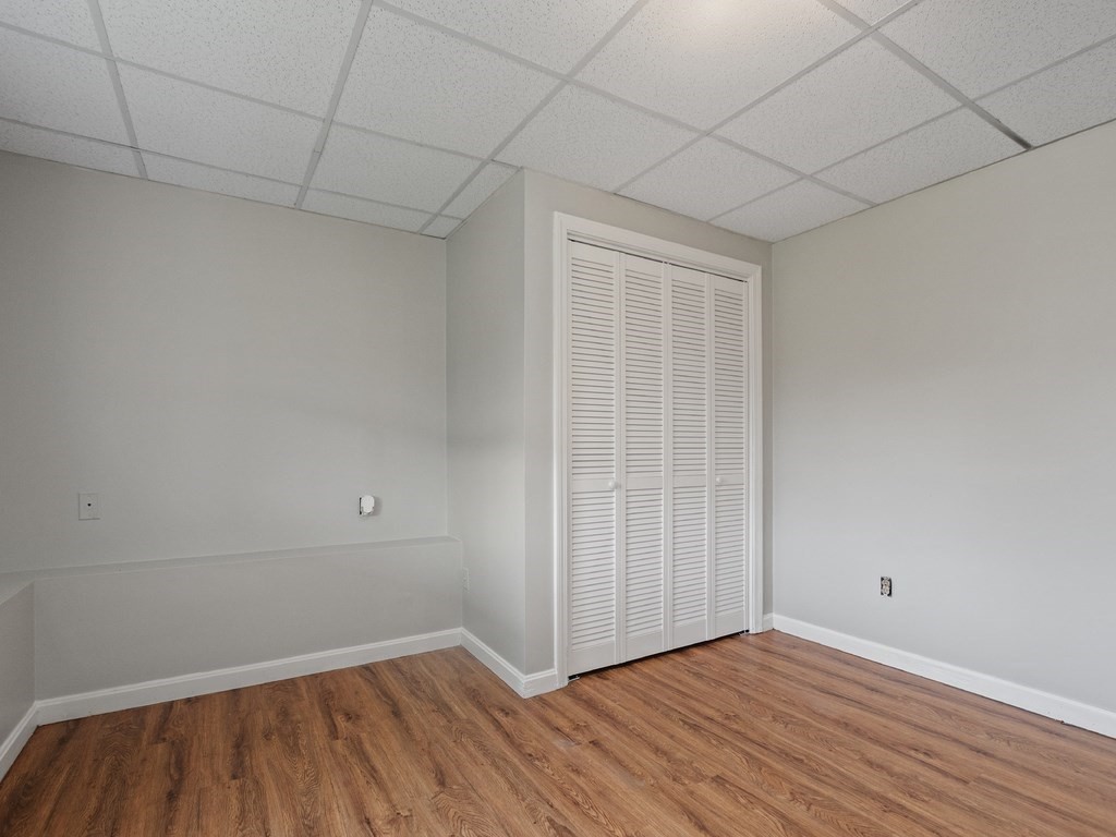 Unfurnished room with louvered closet doors, a drop ceiling, and wood-look flooring.