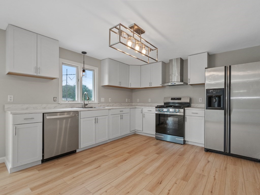 Modern kitchen with white cabinets, stainless steel appliances, and light wood flooring.