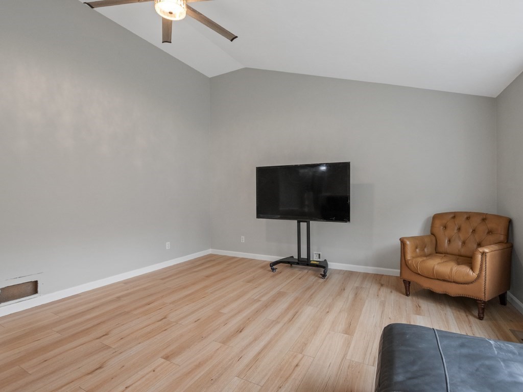 Living room with light wood-look floors, a vaulted ceiling, television, and brown leather armchair.