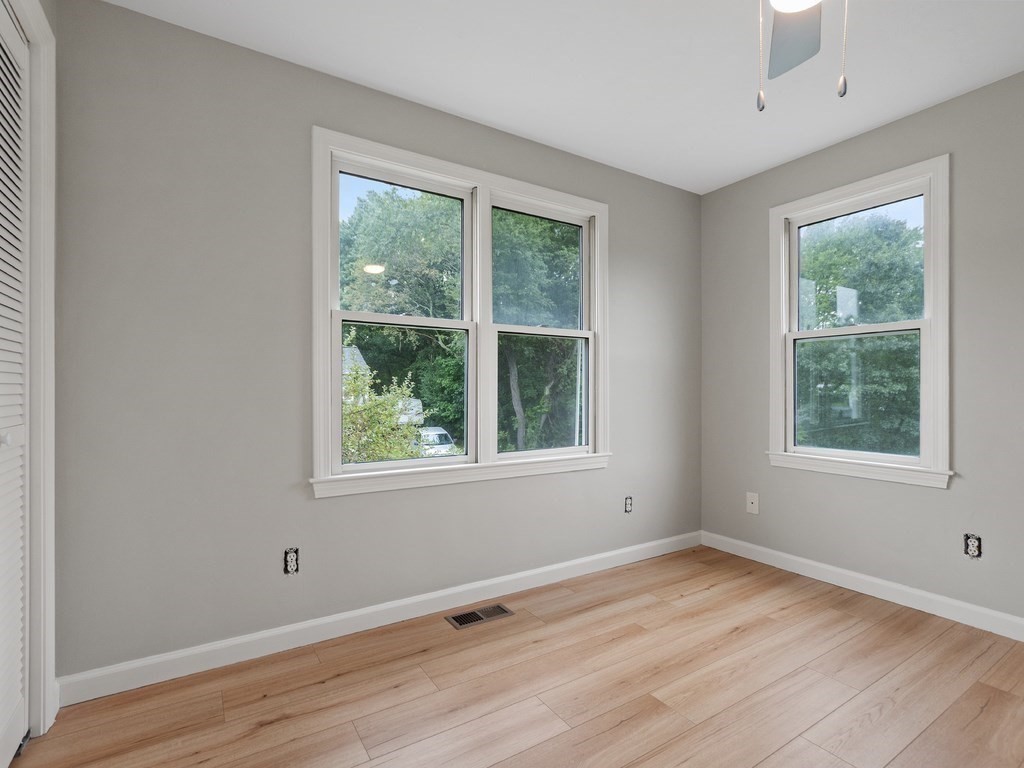Empty room with pale wood floors, gray walls, and three white-trimmed windows.