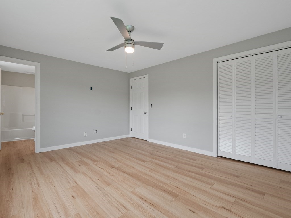 Vacant bedroom with light wood flooring, a ceiling fan, and louvered closet doors.