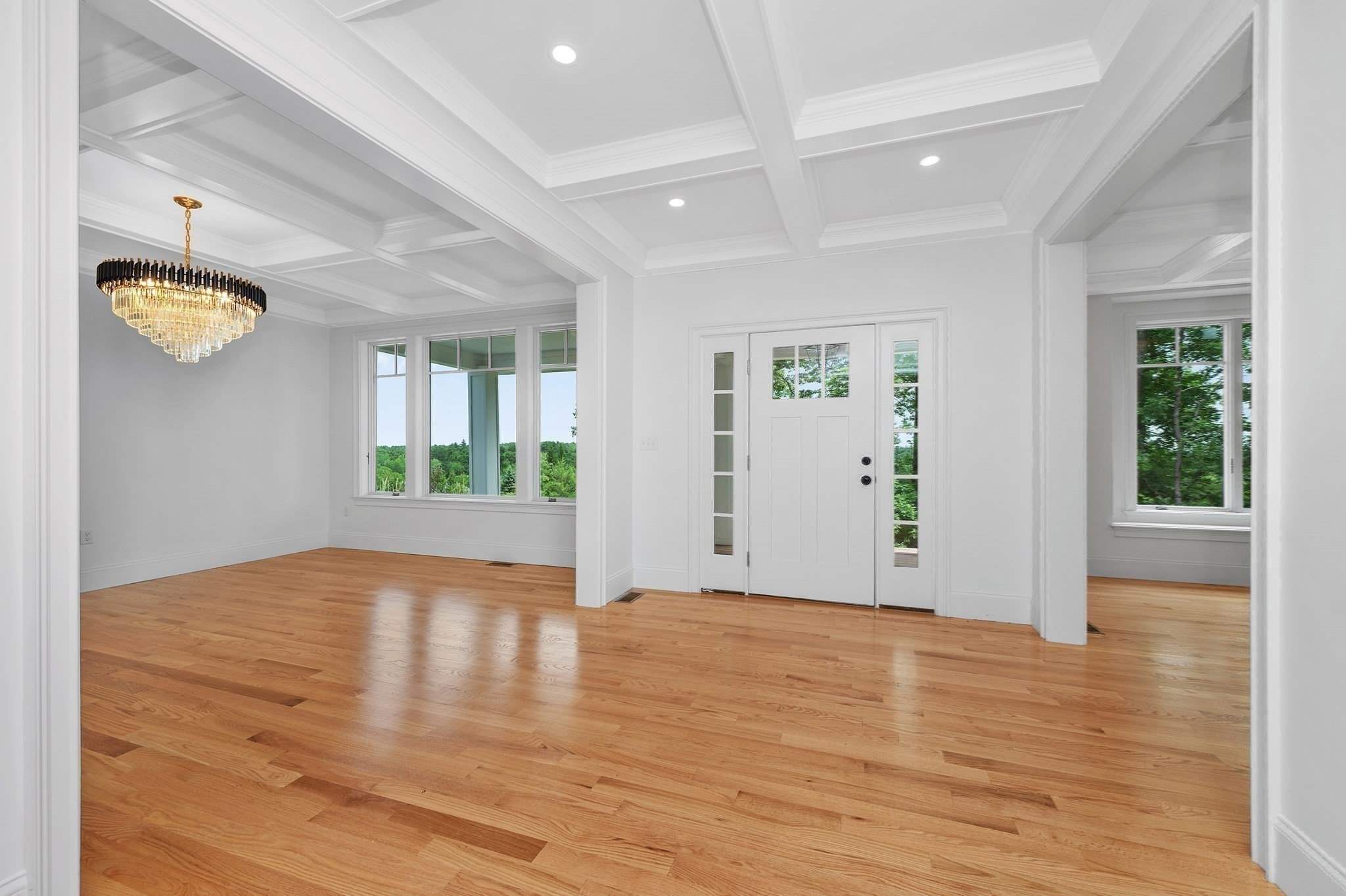 Empty entry hall with a white front door, coffered ceiling, hardwood floors, and chandelier.