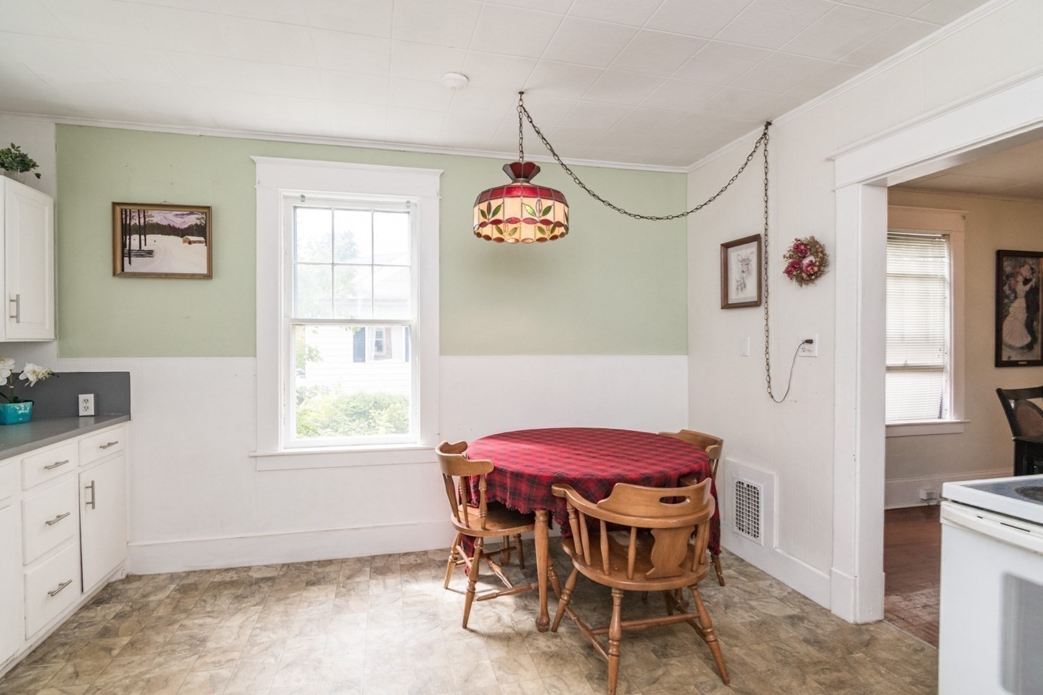 Dining area with a red plaid tablecloth, wooden chairs, and stained-glass pendant light.