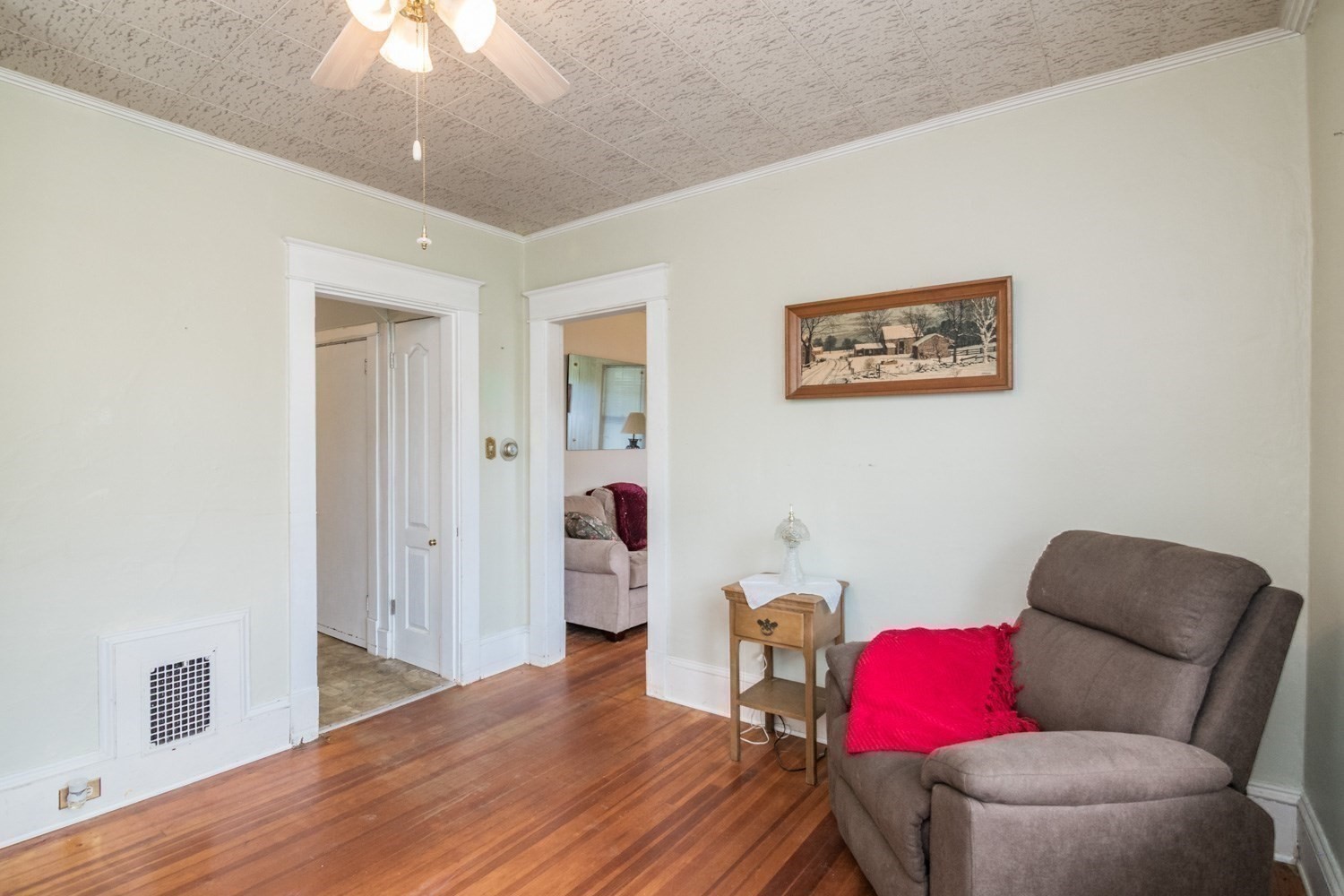 Sitting room with hardwood floors, gray recliner, bright red throw, and two doorways to adjoining rooms.
