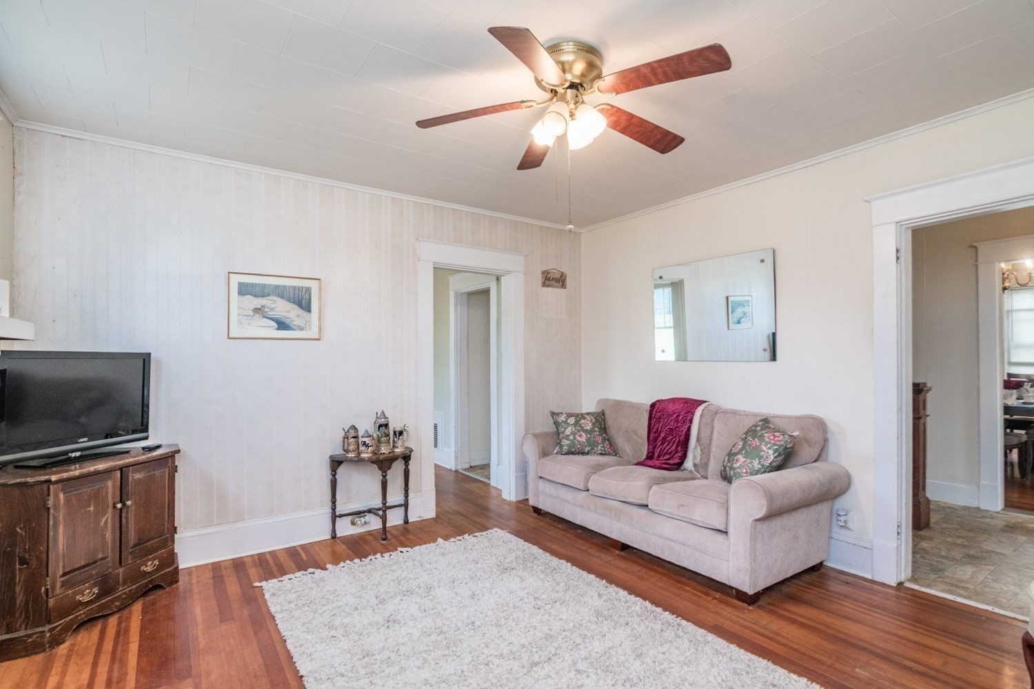 Living room with a beige sofa, polished hardwood floors, and a ceiling fan.
