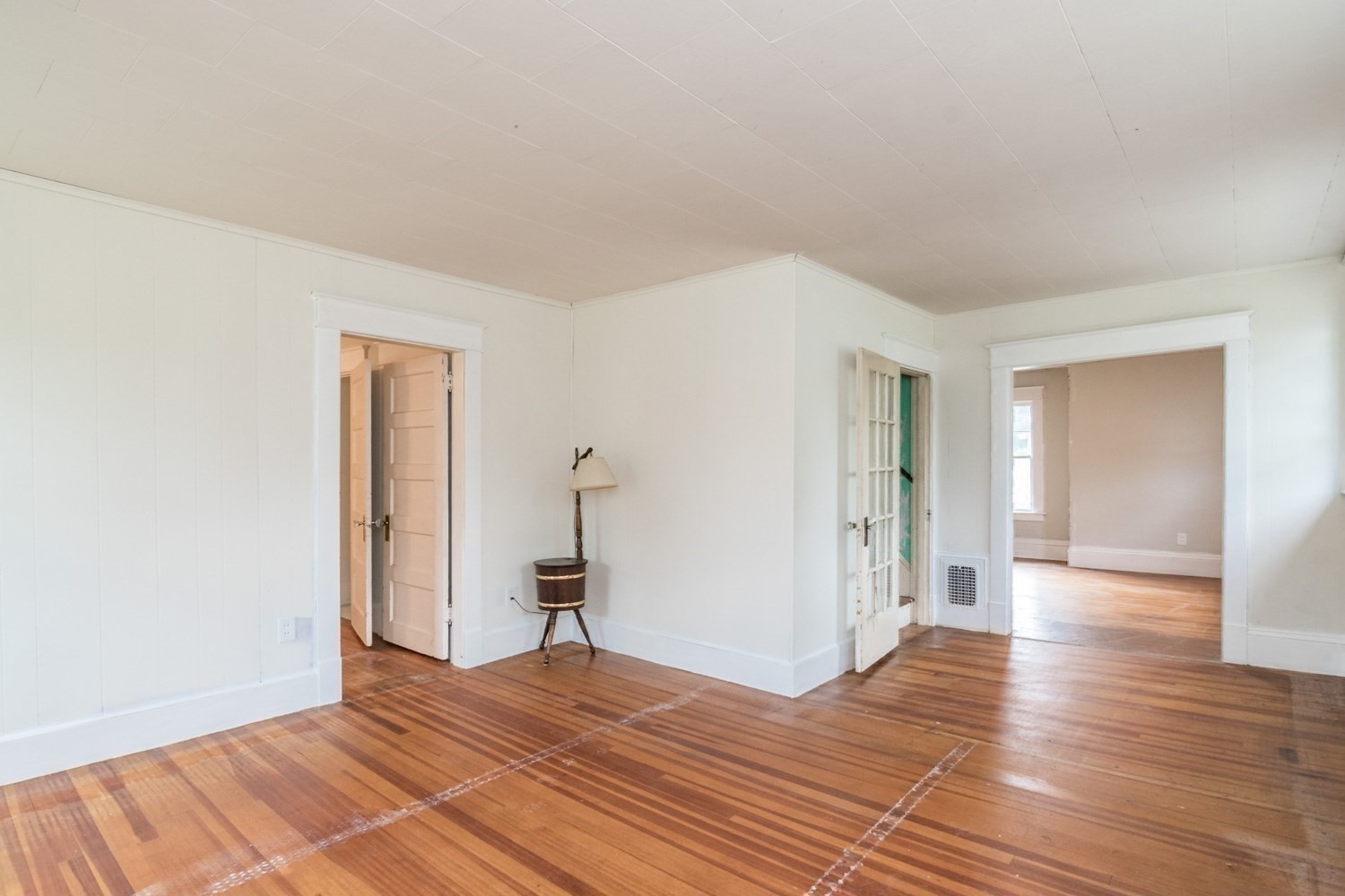 Empty room with polished hardwood floors, white paneled walls, and open doorways to adjoining rooms.