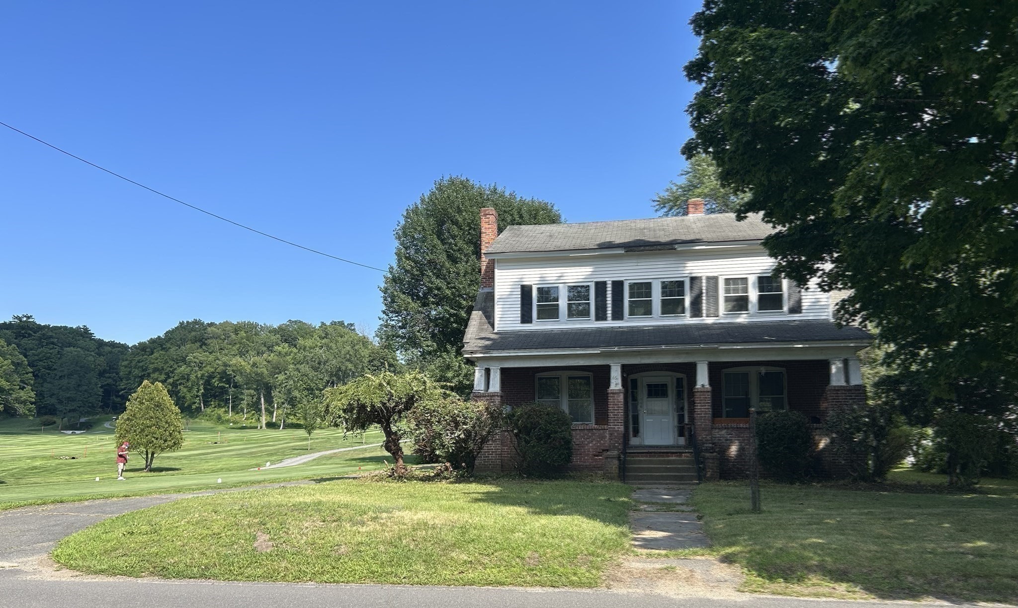 Two-story white-and-brick house with a covered porch beside a golf course.