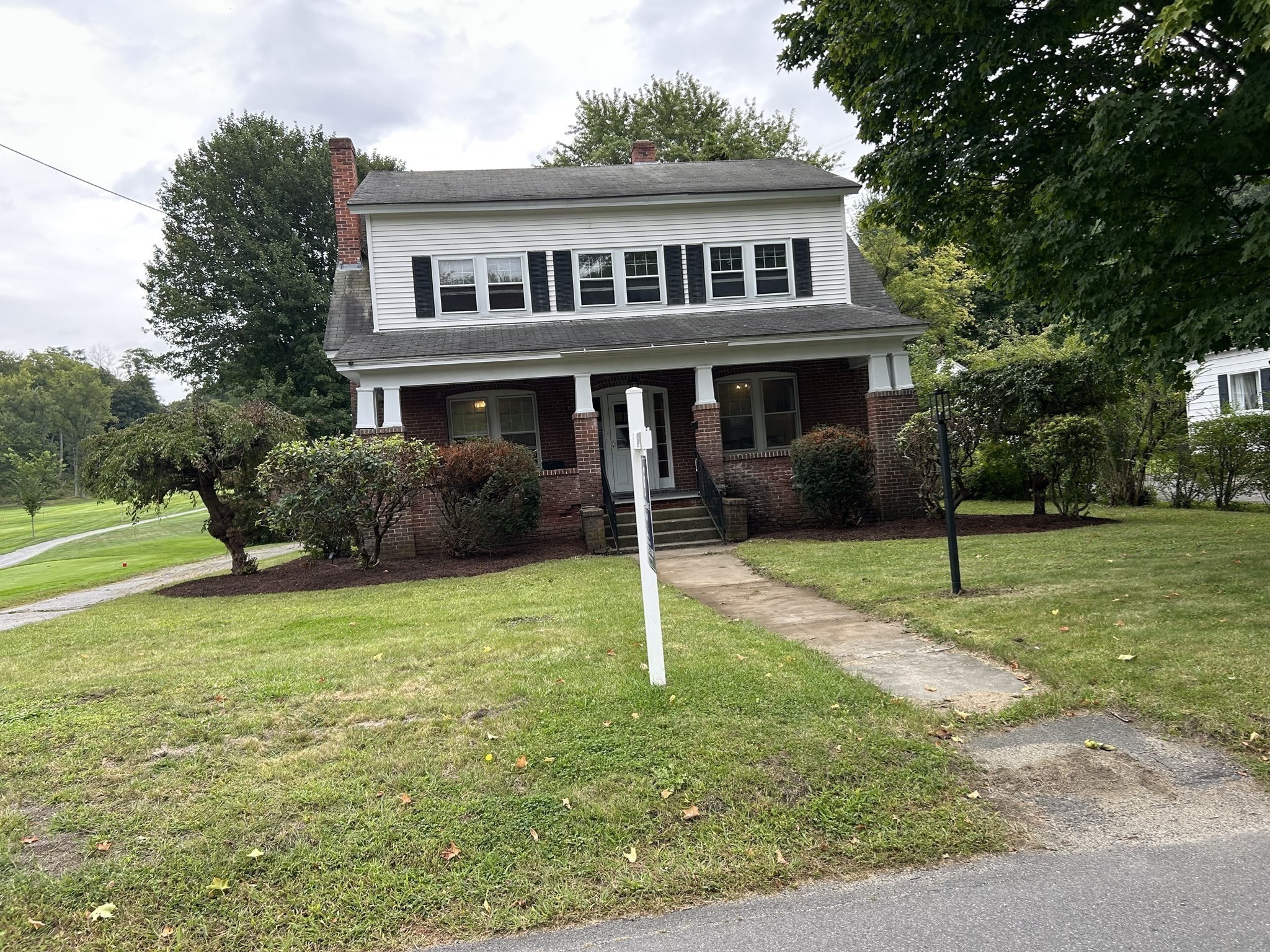 Two-story white-sided and red-brick house with a covered porch, lawn, and fairway beside it.