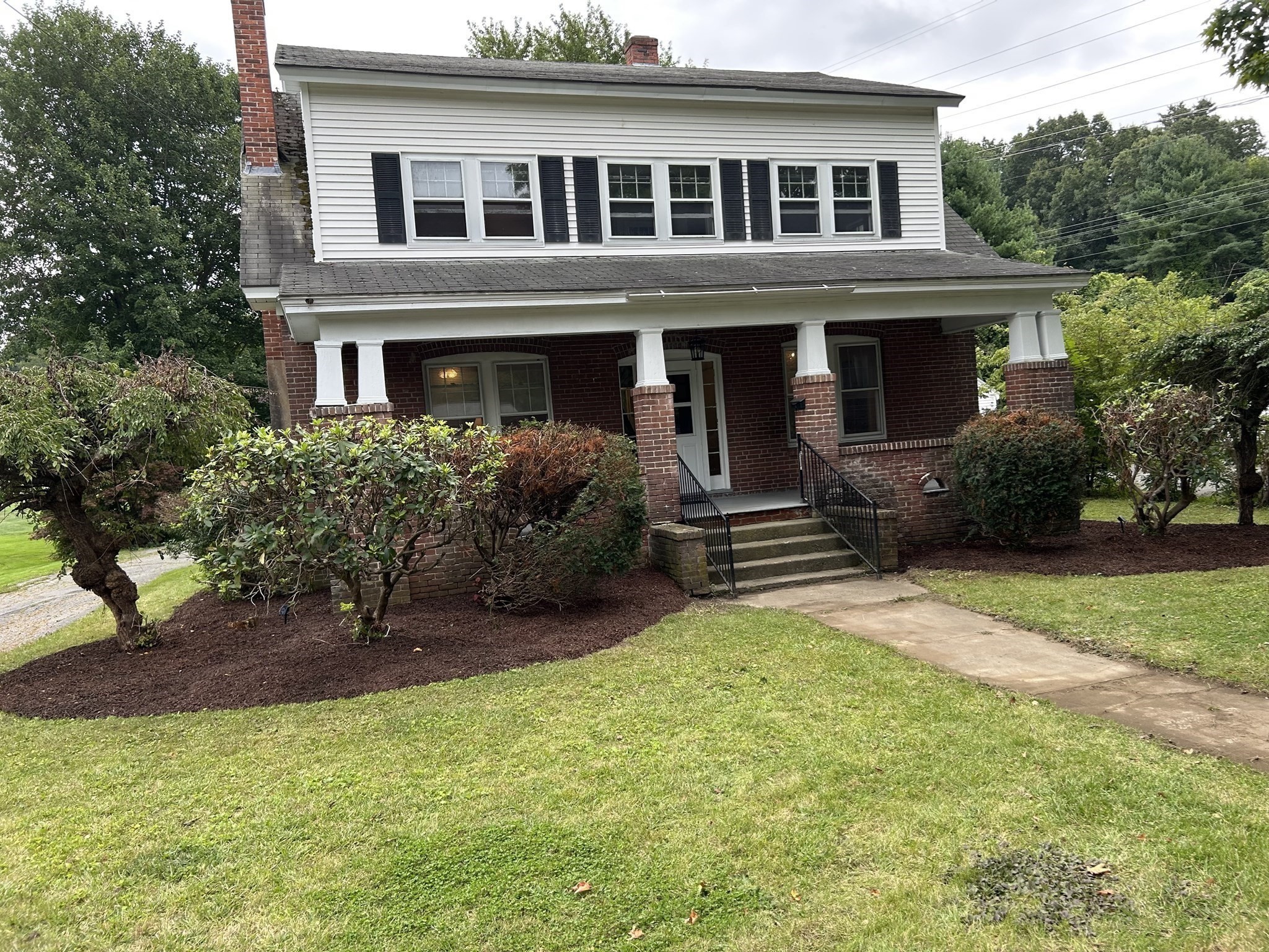 Two-story brick and white-sided house with a covered porch, front steps, and landscaped lawn.