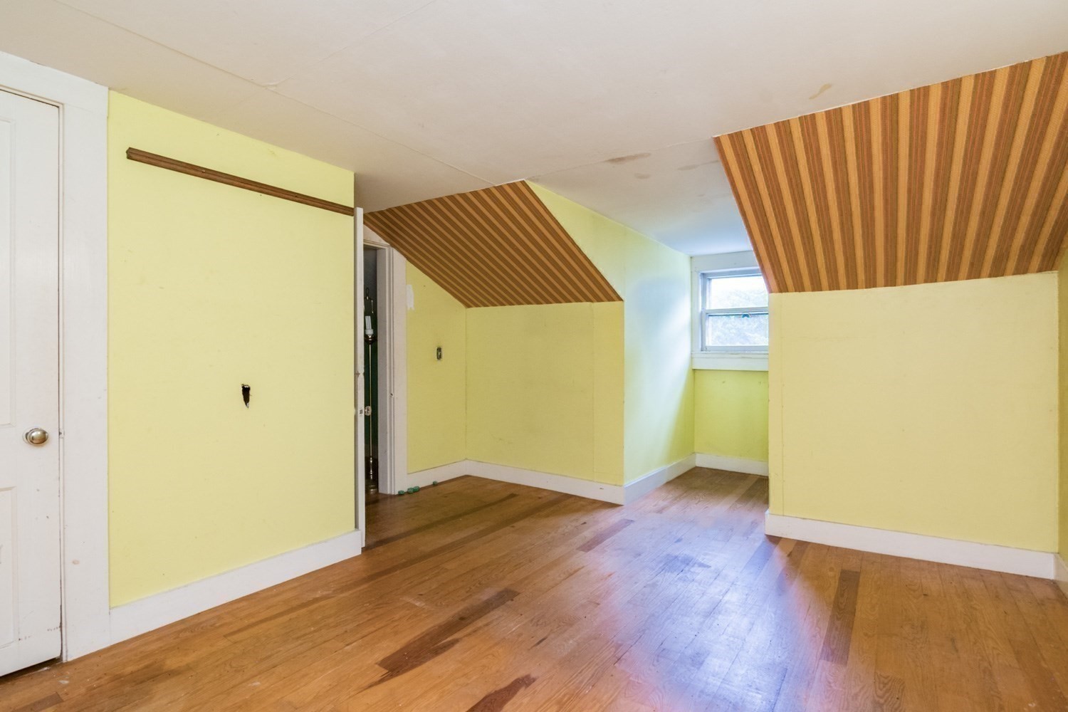 Vacant room with hardwood floors, yellow walls, and angled striped wood ceiling panels.