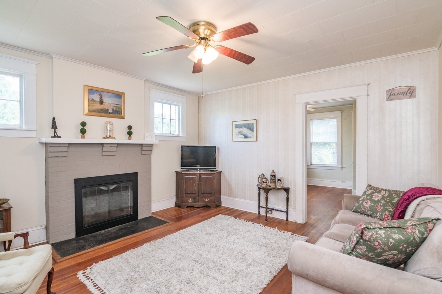 Living room with a white brick fireplace, hardwood floors, and a ceiling fan.