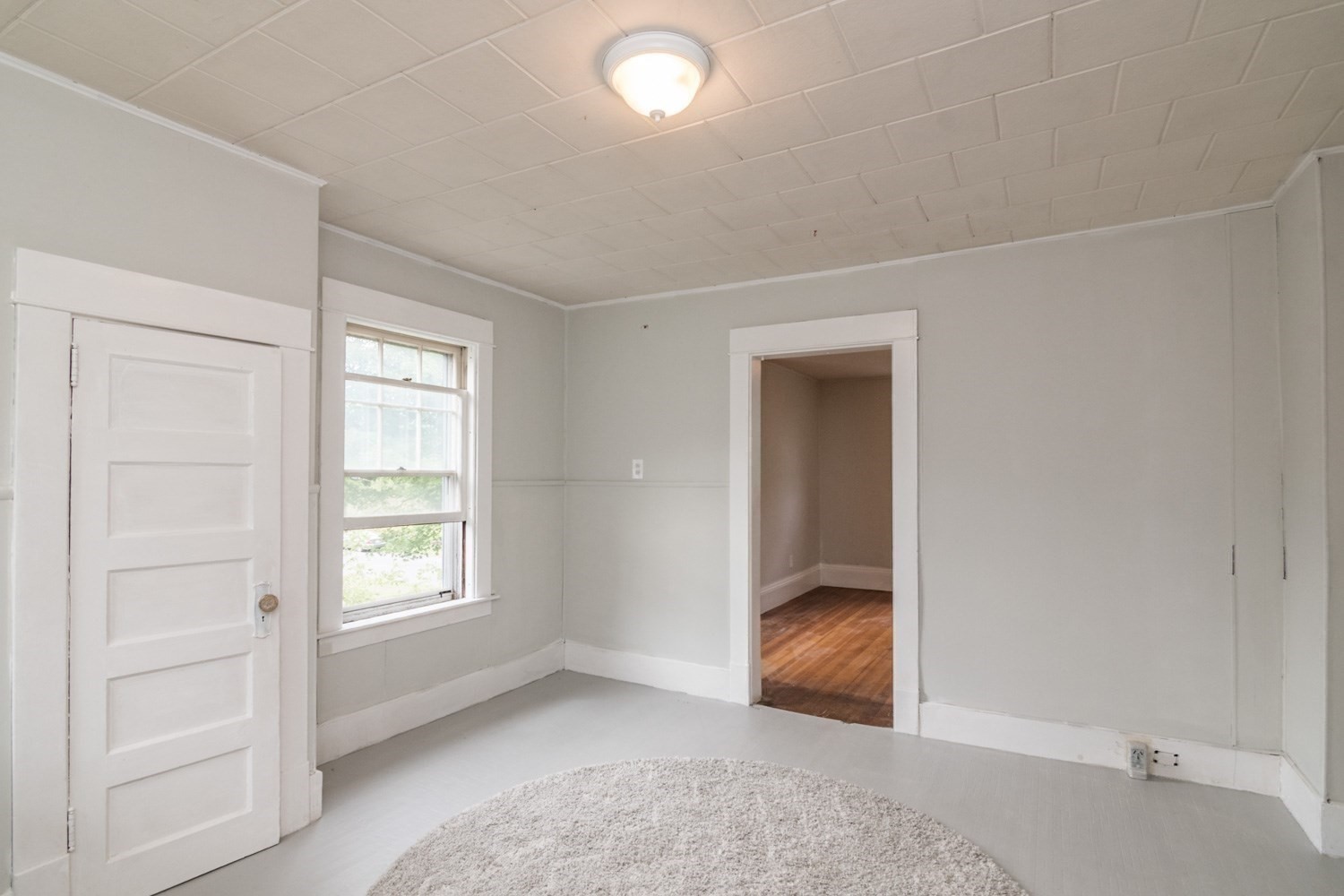 Empty room with a paneled door, window, and doorway to a hardwood-floored room.