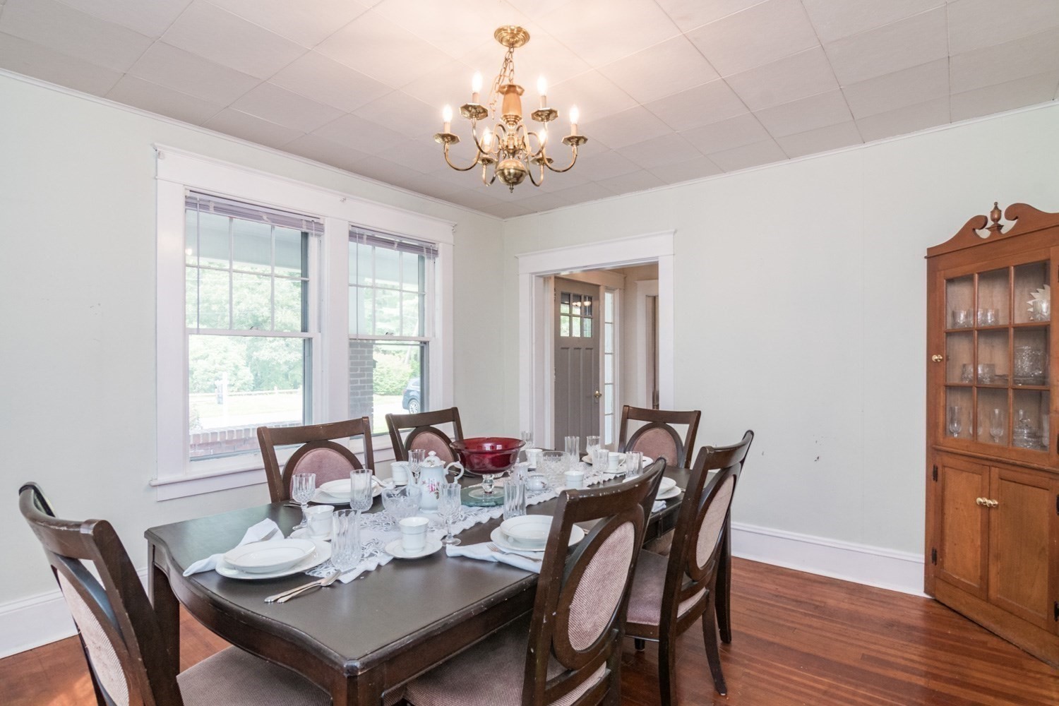 Dining room with a set table, upholstered chairs, brass chandelier, and glass-front china cabinet.