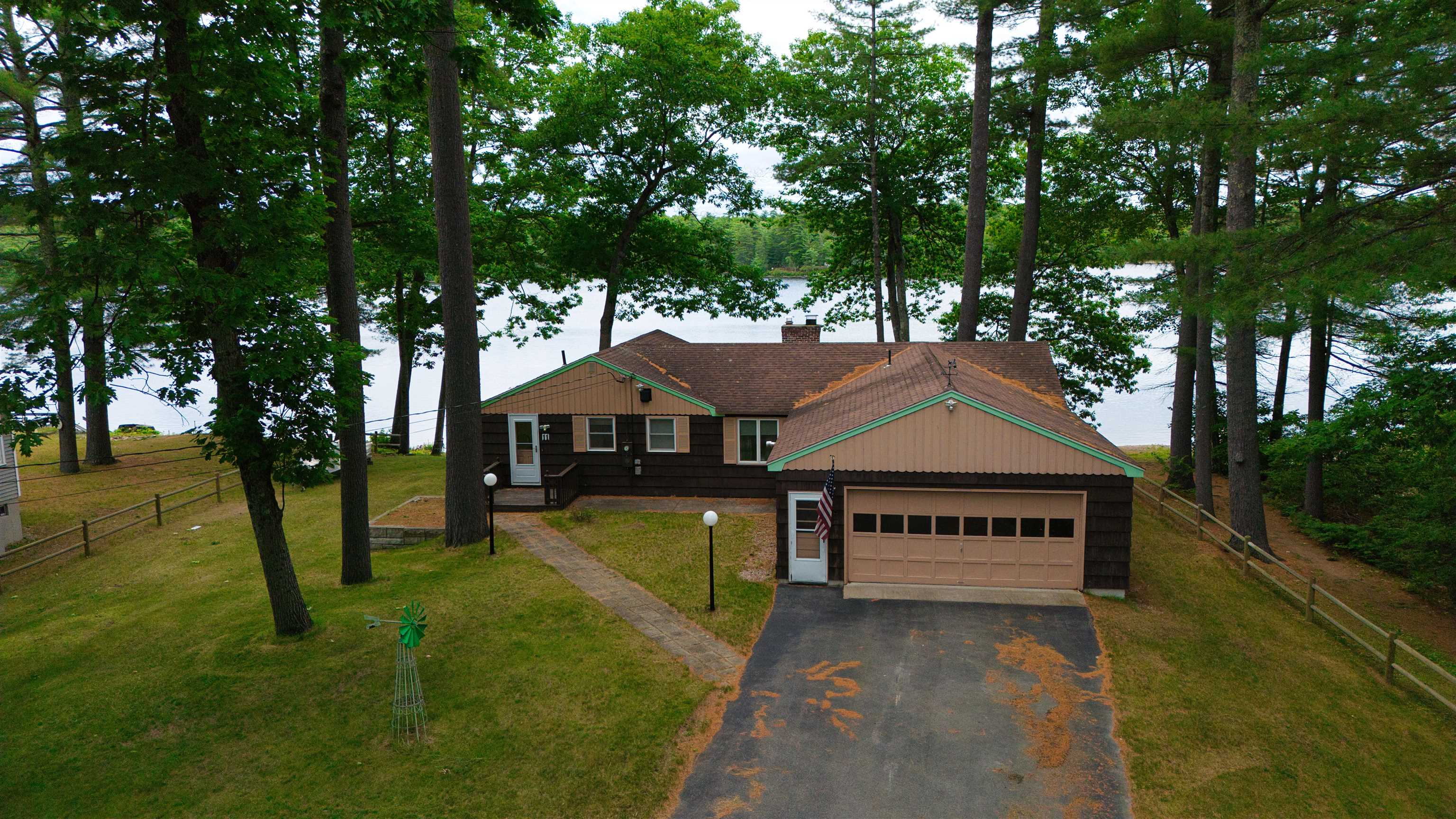Lakefront home among mature trees, with a tan garage and the water visible behind it.