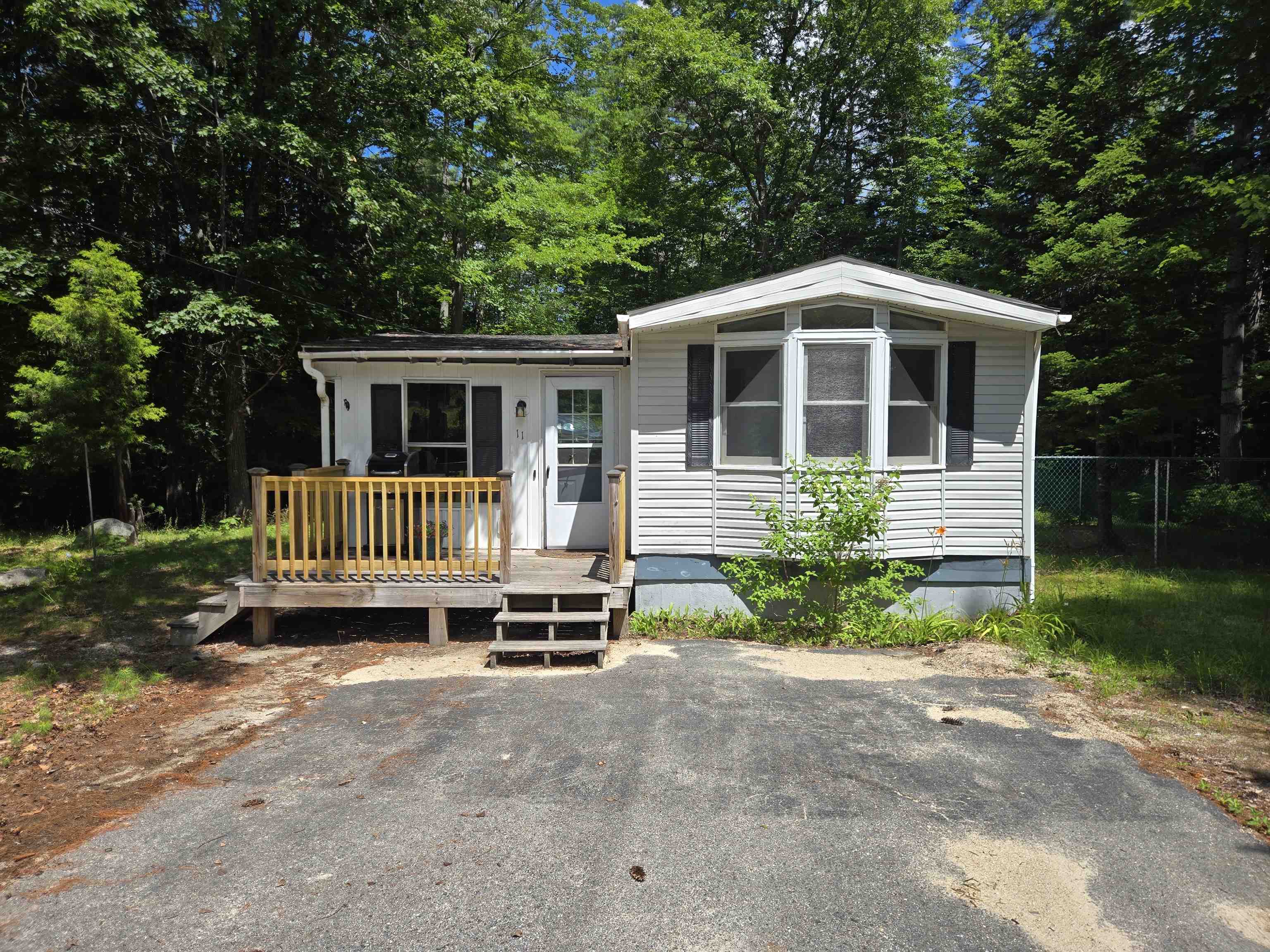 White single-story home with a raised wooden deck and bay window in a wooded setting.