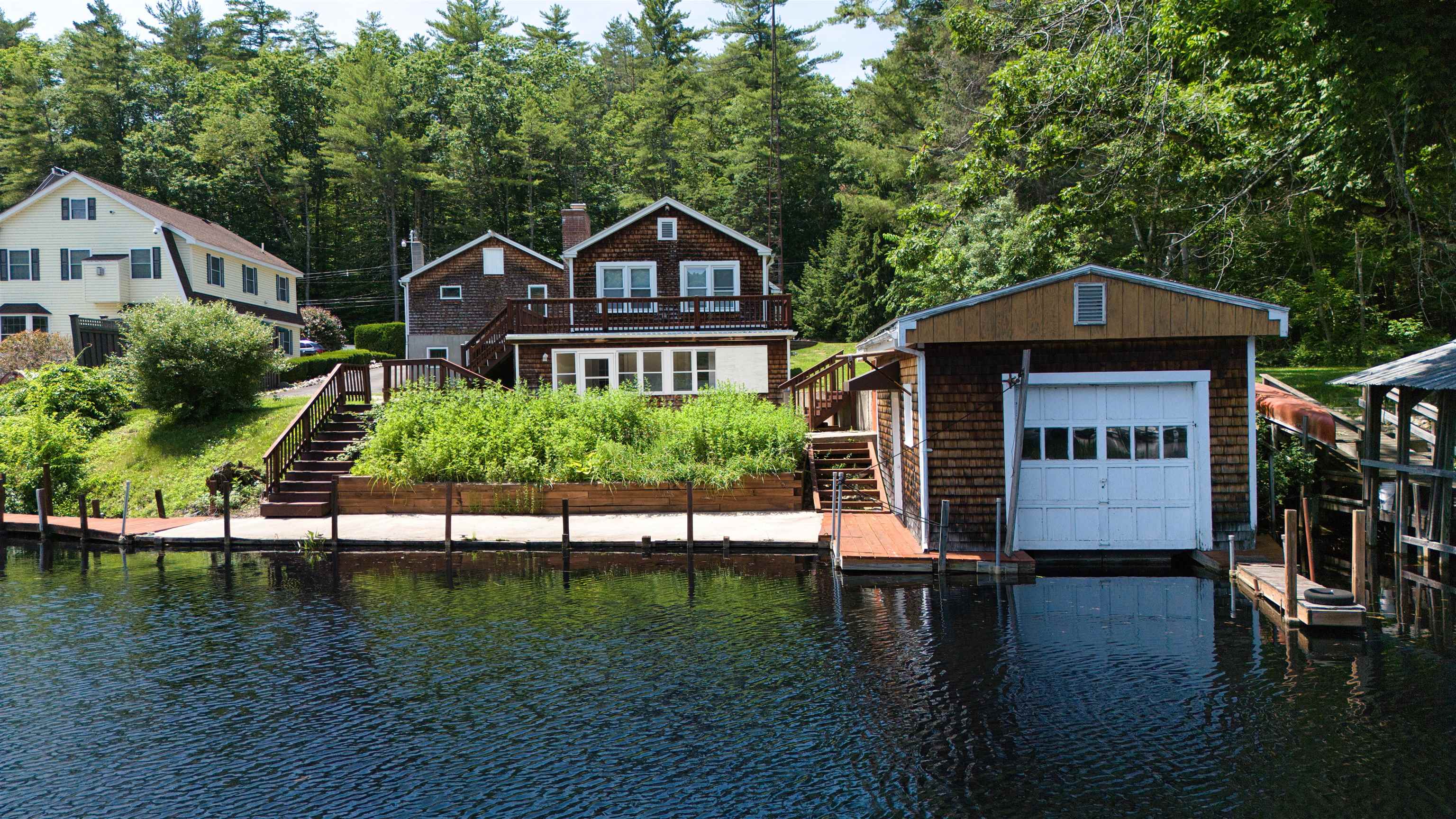 Shingle lakeside home with raised deck, detached boathouse, and docks along the water.