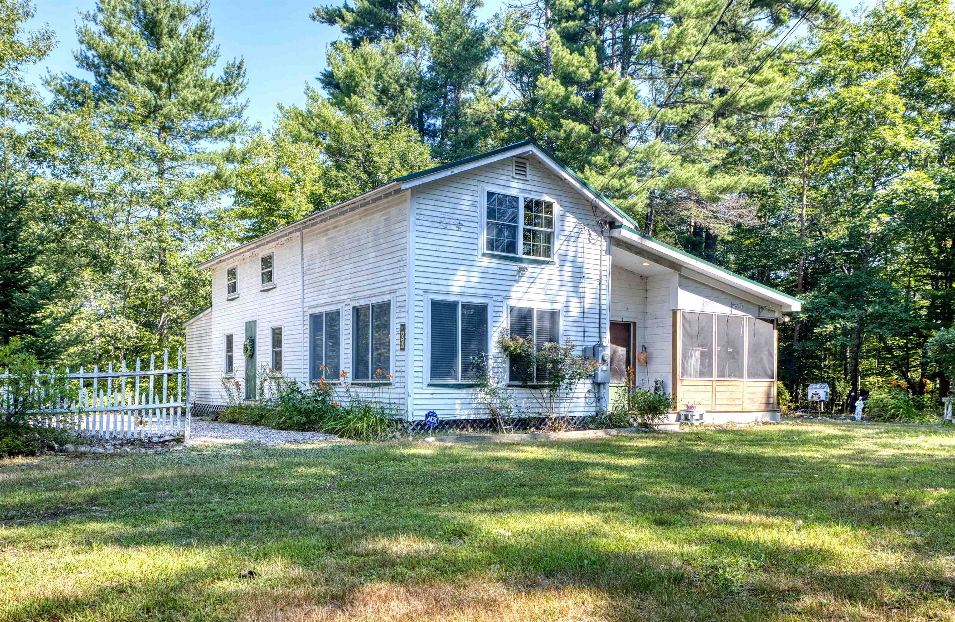 White two-story house with a screened porch, surrounded by trees and a sunny lawn.