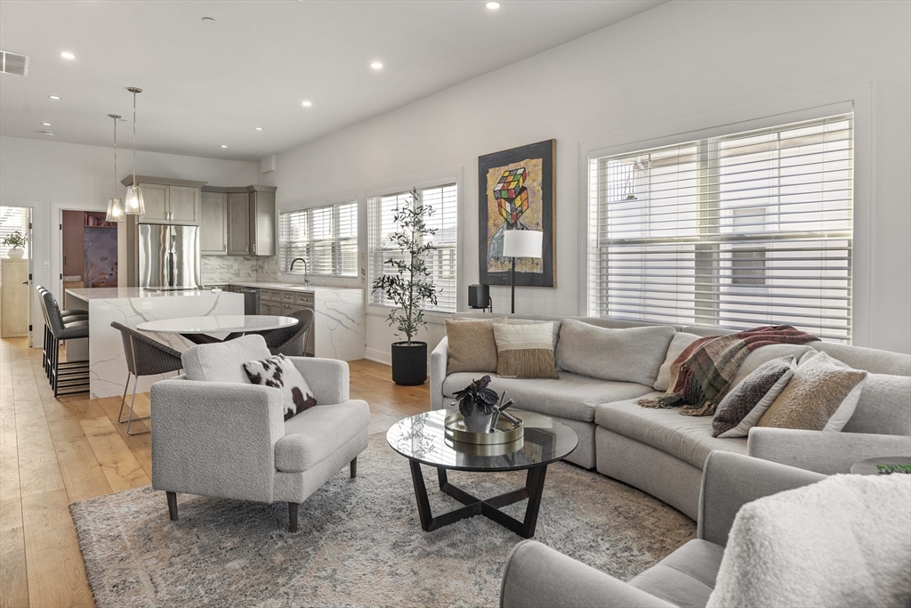 Open-plan living room and kitchen with a gray sectional, marble island, and wide windows.