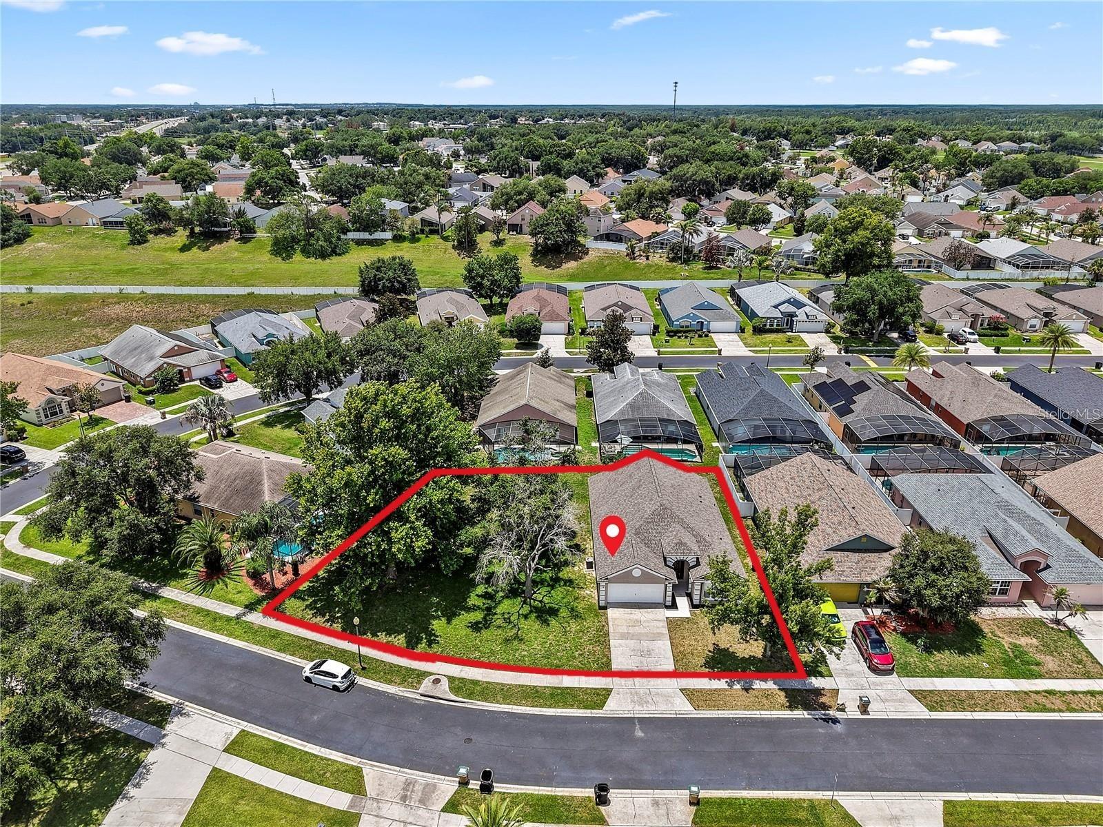 Aerial view of a house on a large corner lot outlined in red, marked with a location pin.