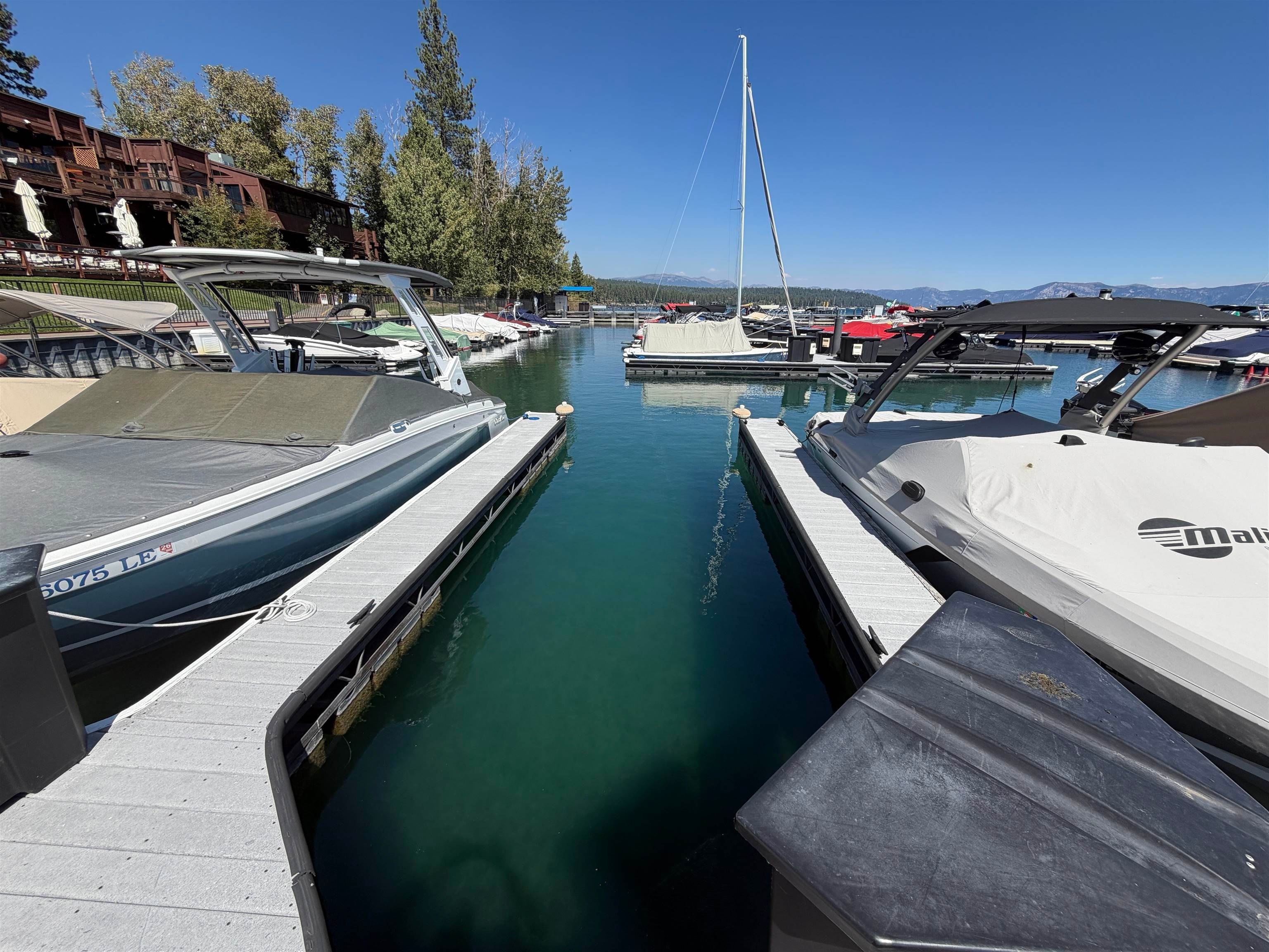 Marina slip between docks, with covered boats, a waterfront lodge, and distant mountains.
