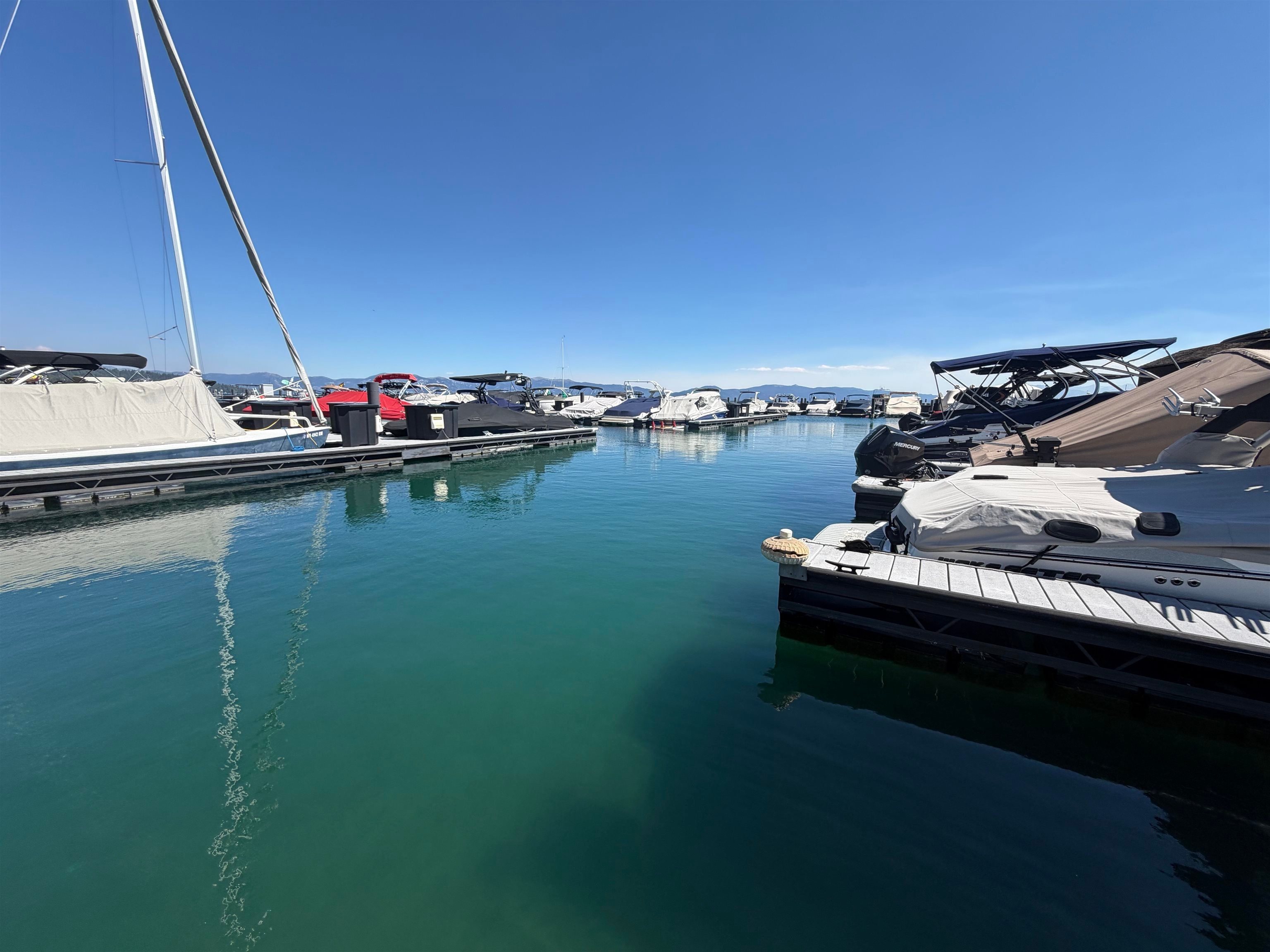 Marina docks lined with covered boats on turquoise water, with mountains in the distance.