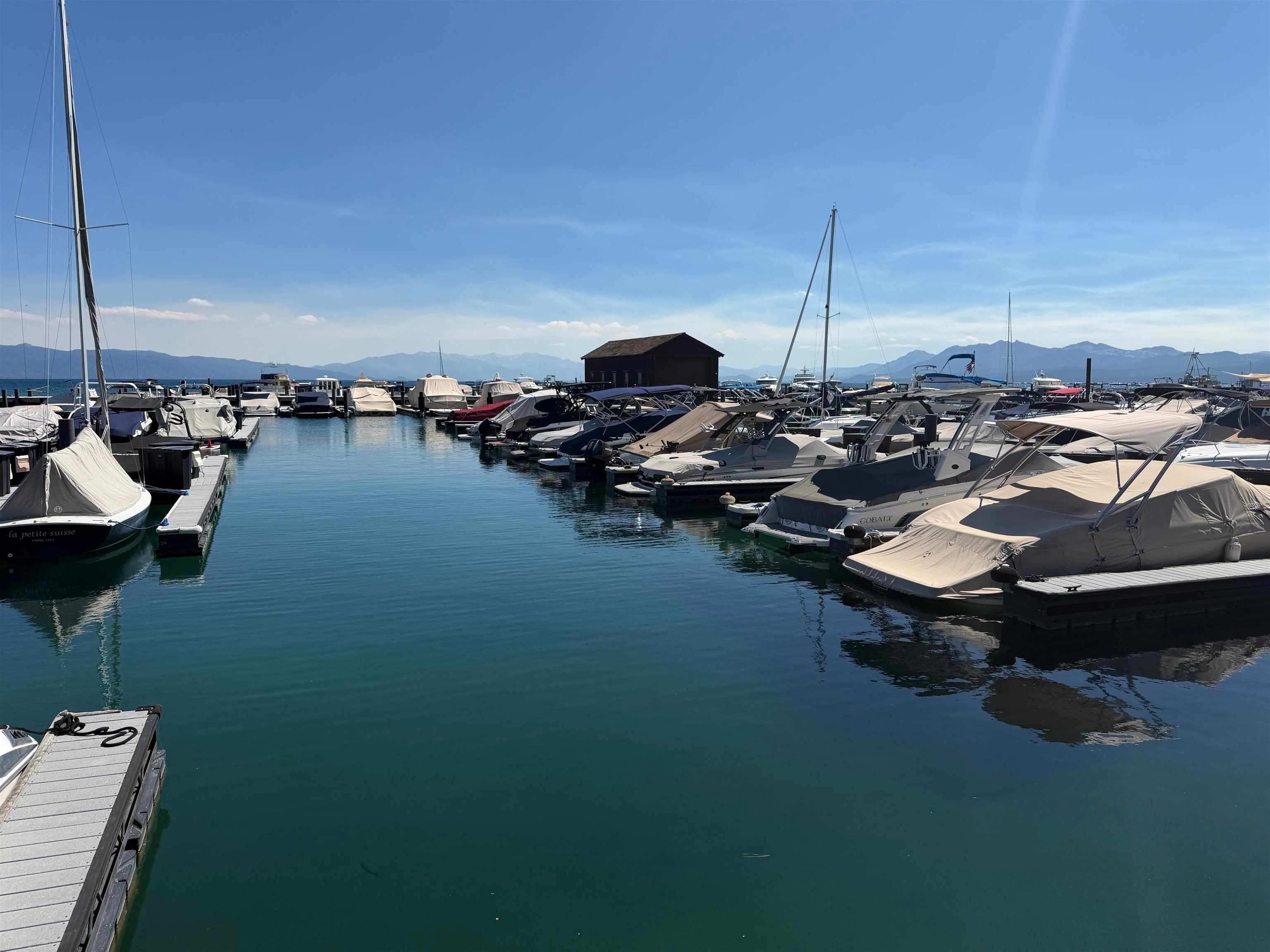 Lake Tahoe marina with moored boats, turquoise water, and mountain ranges in the distance.