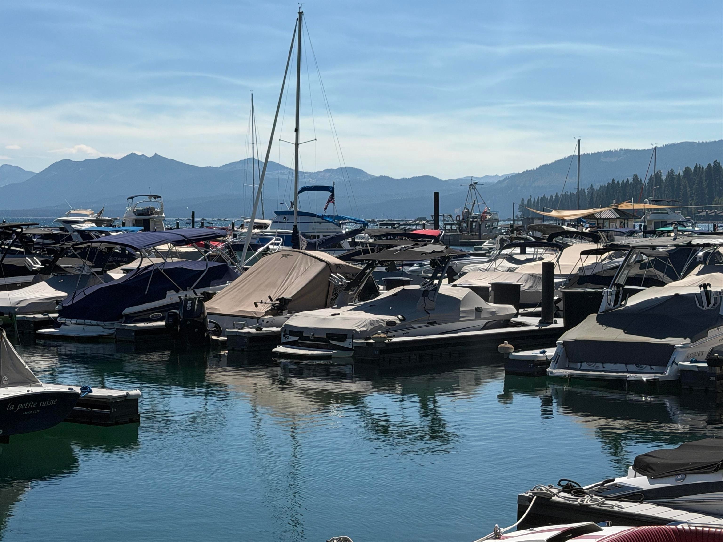 Boats fill a Lake Tahoe marina, with forested mountains beyond the water.