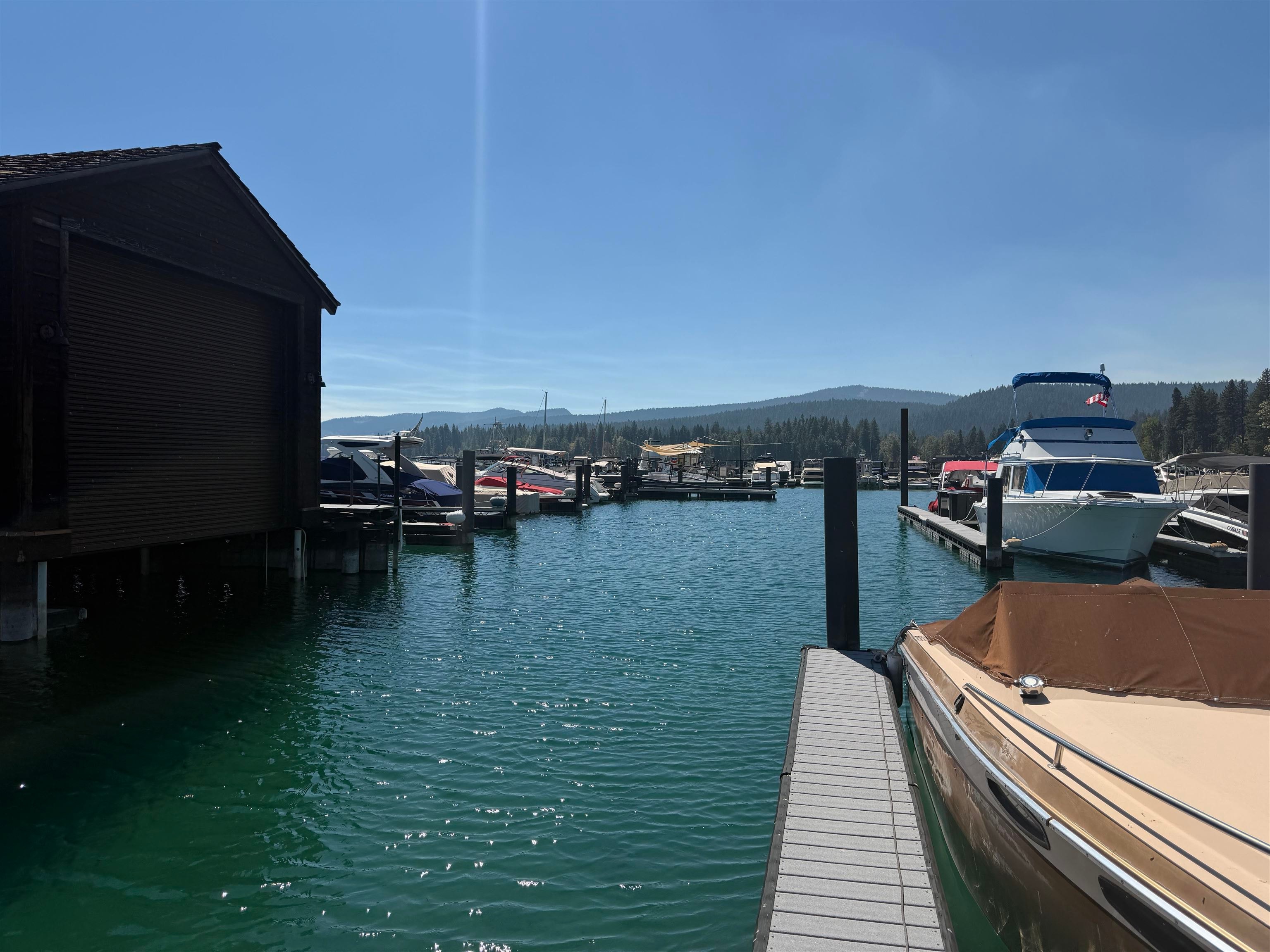 Marina dock with moored boats, a dark boathouse, and forested mountains across the water.