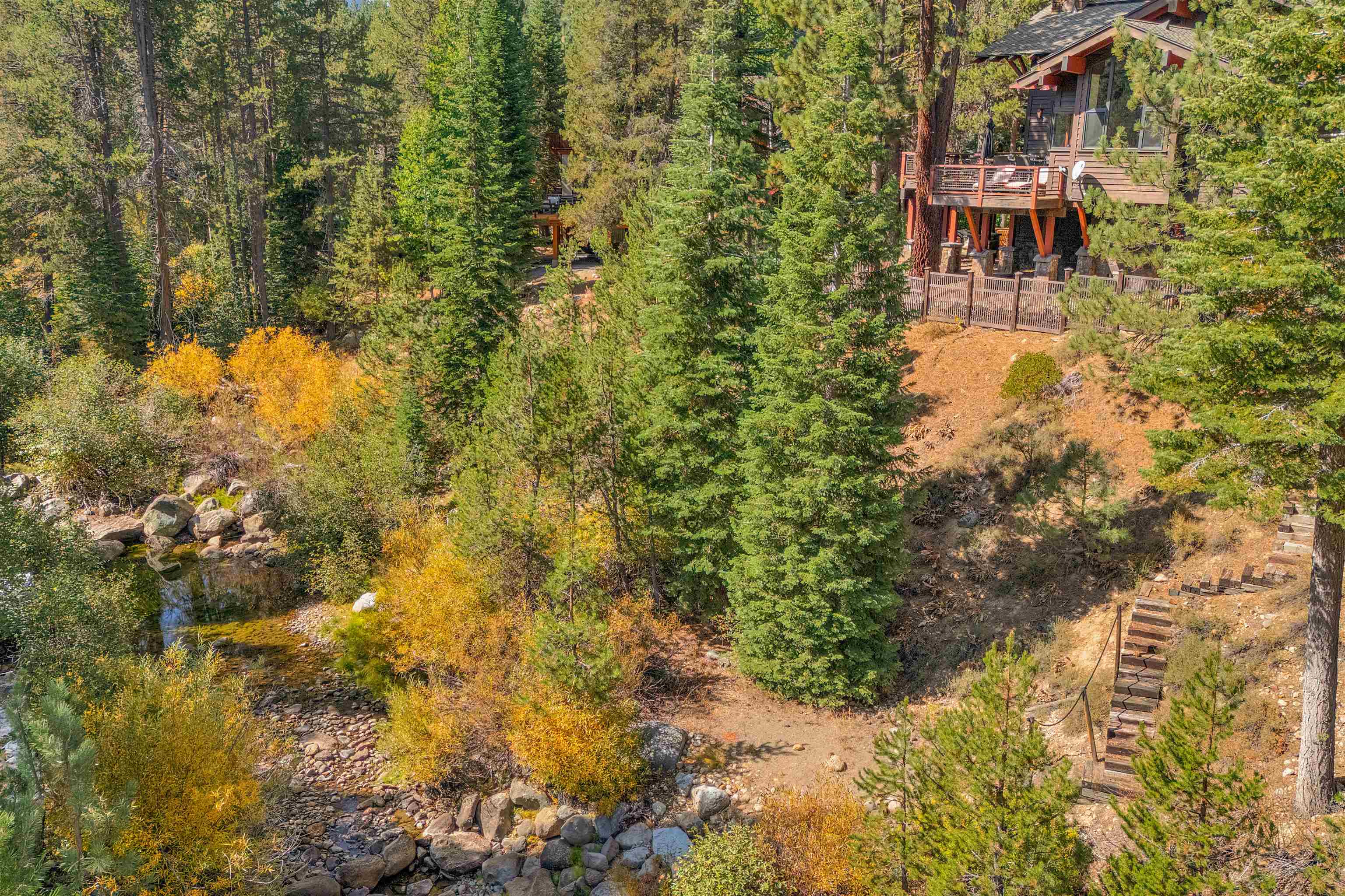 Wooded hillside home above a rocky creek, with a raised deck and stairs.