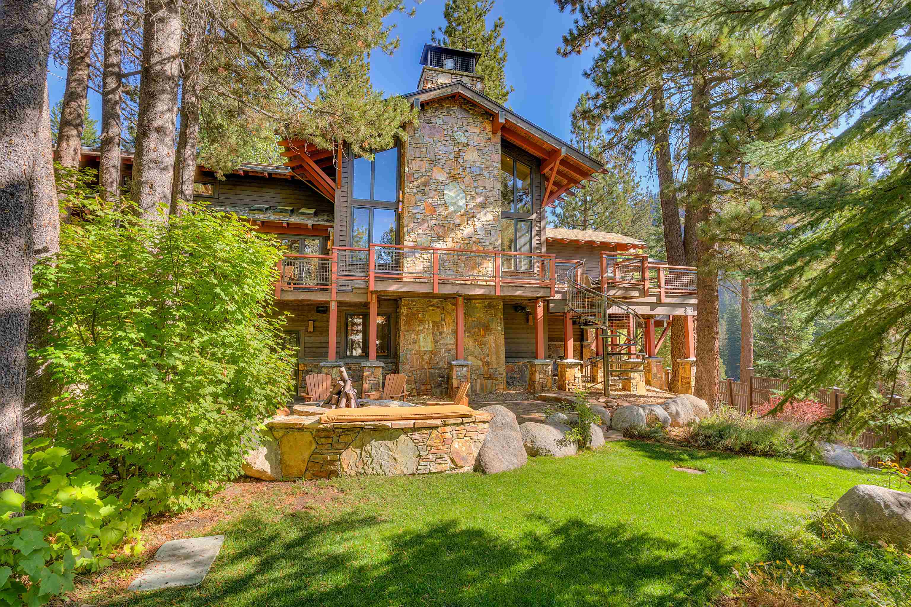 Stone and timber home among pines, with a raised deck, spiral staircase, and stone fire pit.