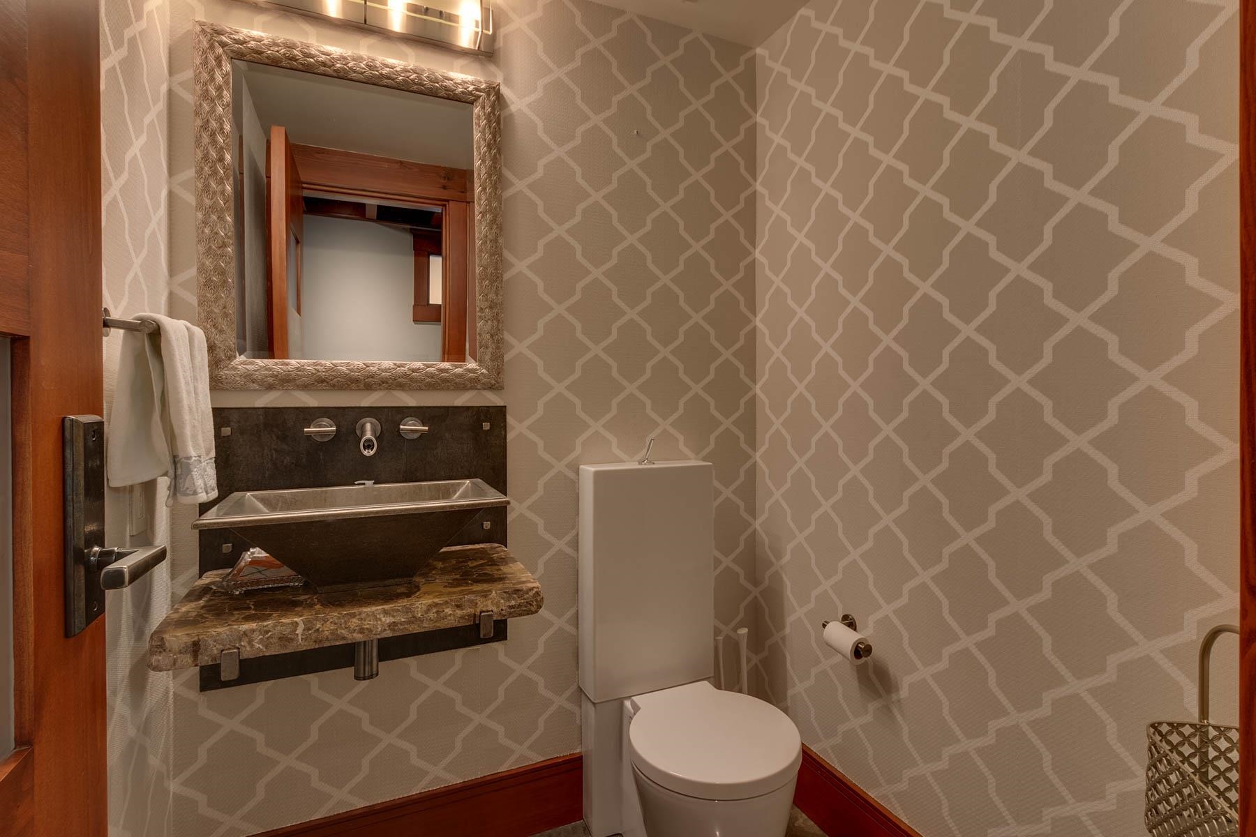 Bathroom with a dark vessel sink, marbled counter, framed mirror, and geometric wallpaper.