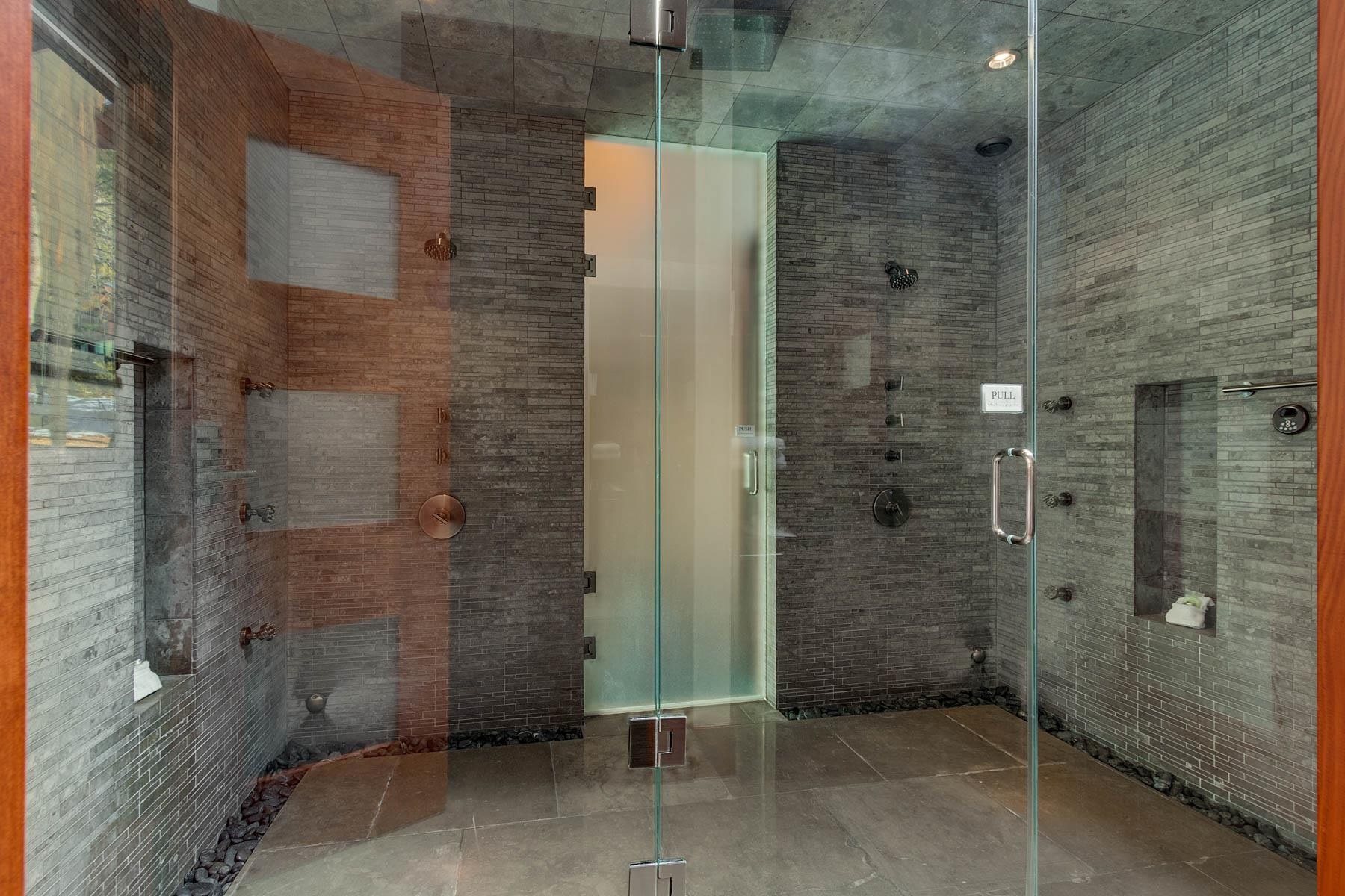 Walk-in shower with gray stone tile, glass doors, two showerheads, and pebble accents.