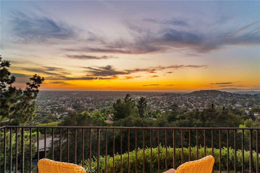 Terrace view over a sprawling city and rolling hills beneath a colorful sunset.