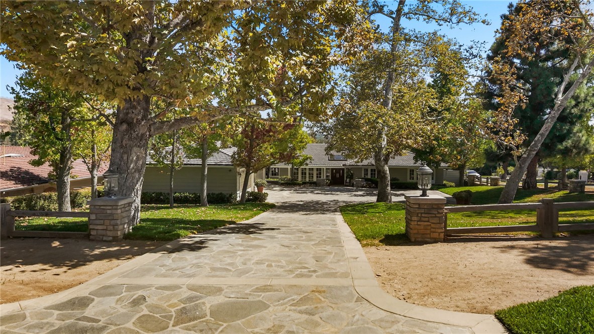 Single-story home behind a stone-paved driveway and mature trees.