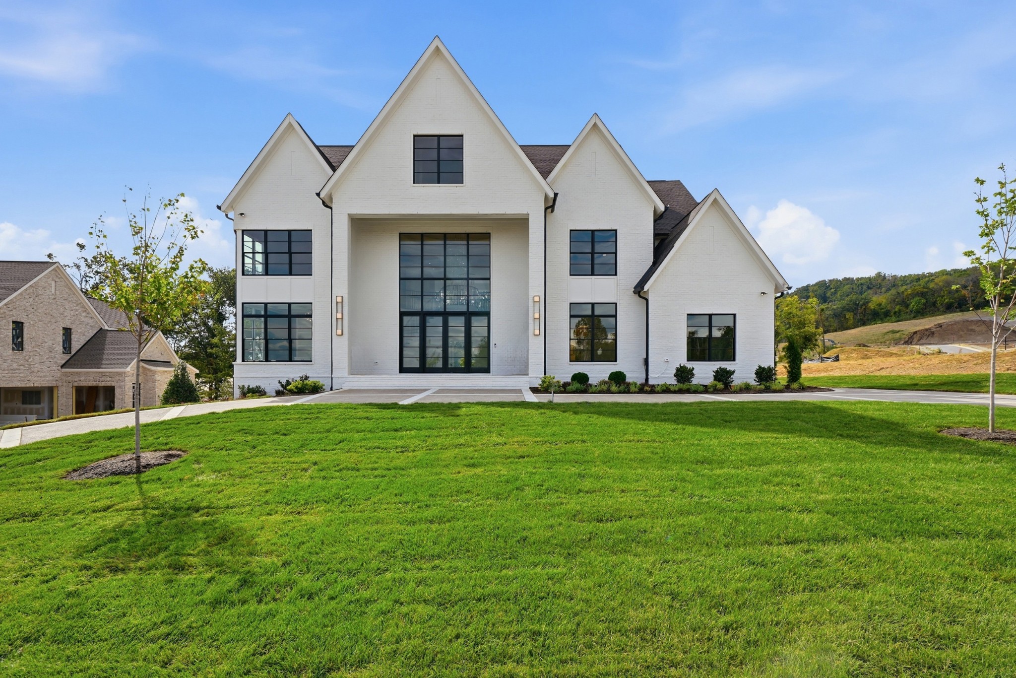 White brick home with steep gables, dark-framed windows, and a broad green lawn.