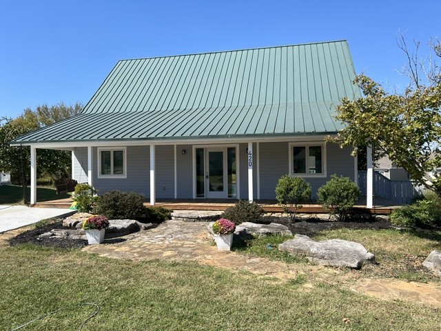 Gray house with a tall green metal roof, white porch posts, and a stone walkway.