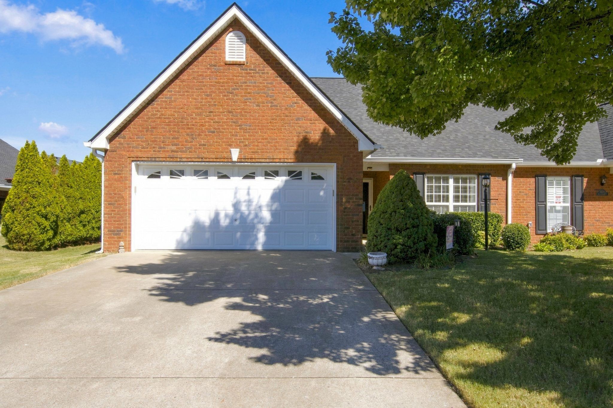 Red brick house with a white double garage, broad driveway, and mature trees shading the lawn.
