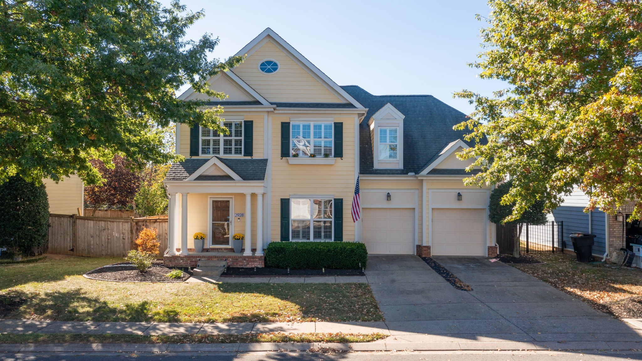 Two-story pale yellow house with dark shutters, a front porch, and a two-car garage.