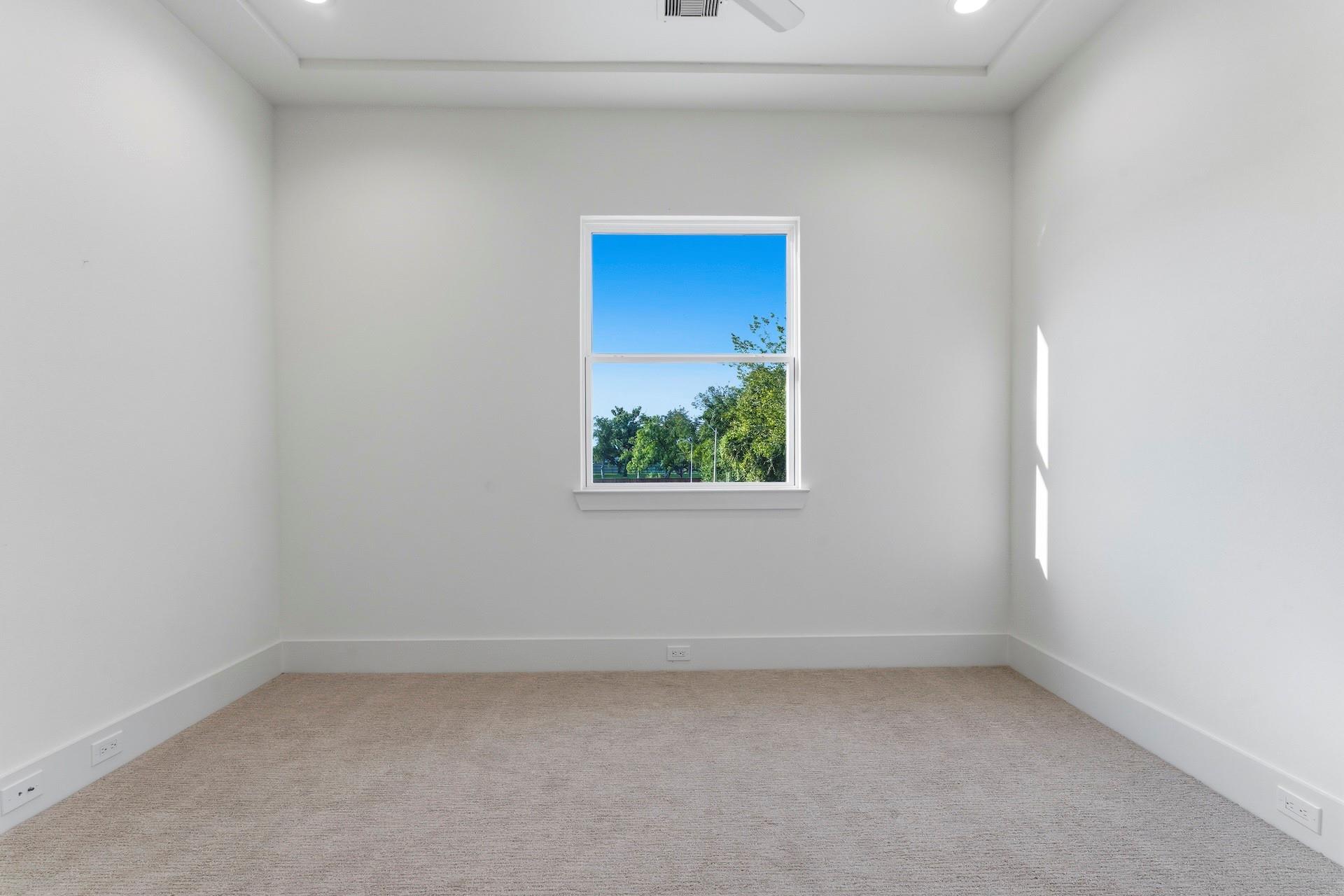 Empty carpeted room with a ceiling fan and a window overlooking trees.