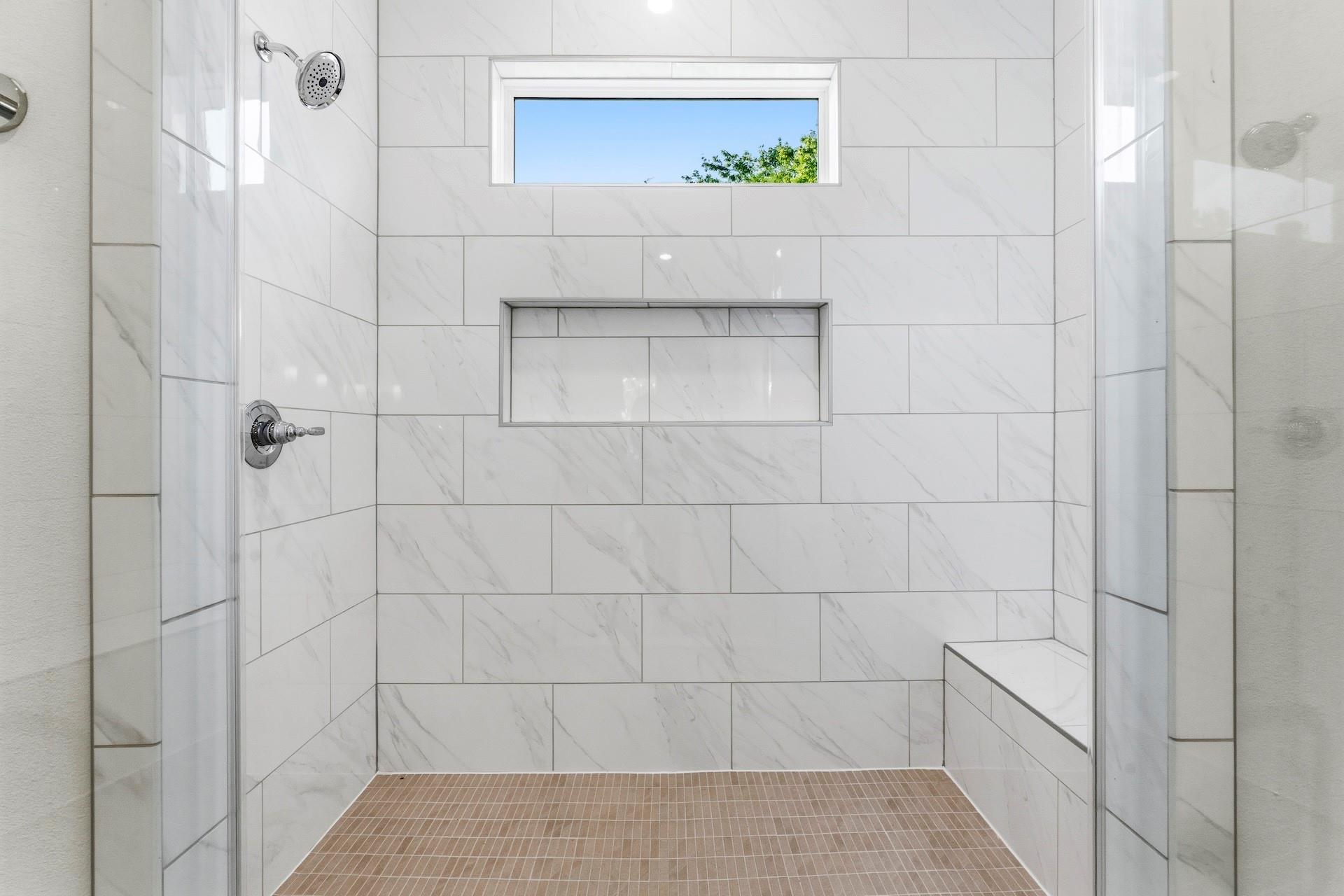 Walk-in shower with white marble-look tile, a built-in niche, tiled bench, and narrow high window.