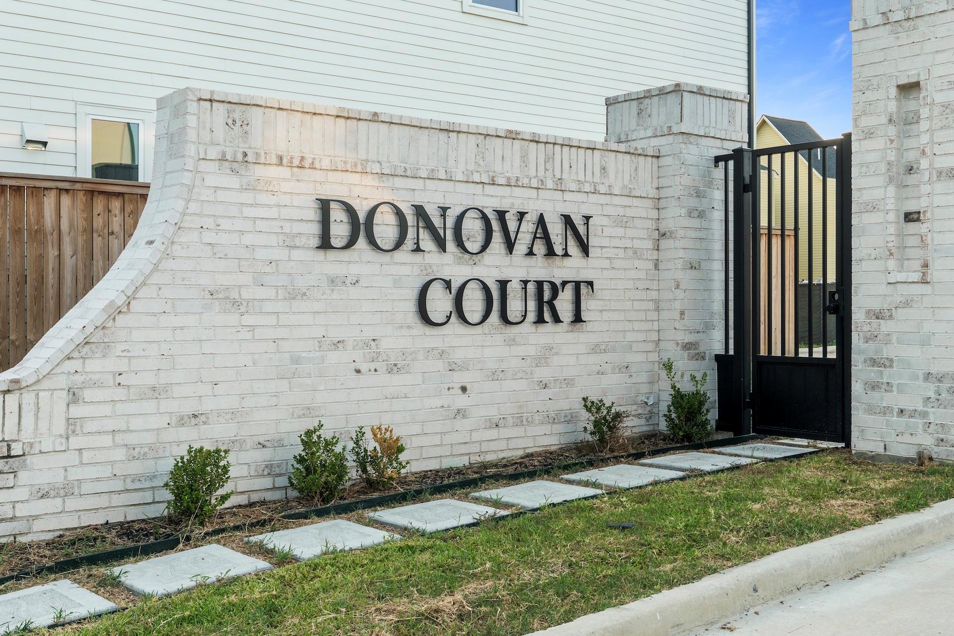Donovan Court entrance sign on a white brick wall beside a black metal gate.