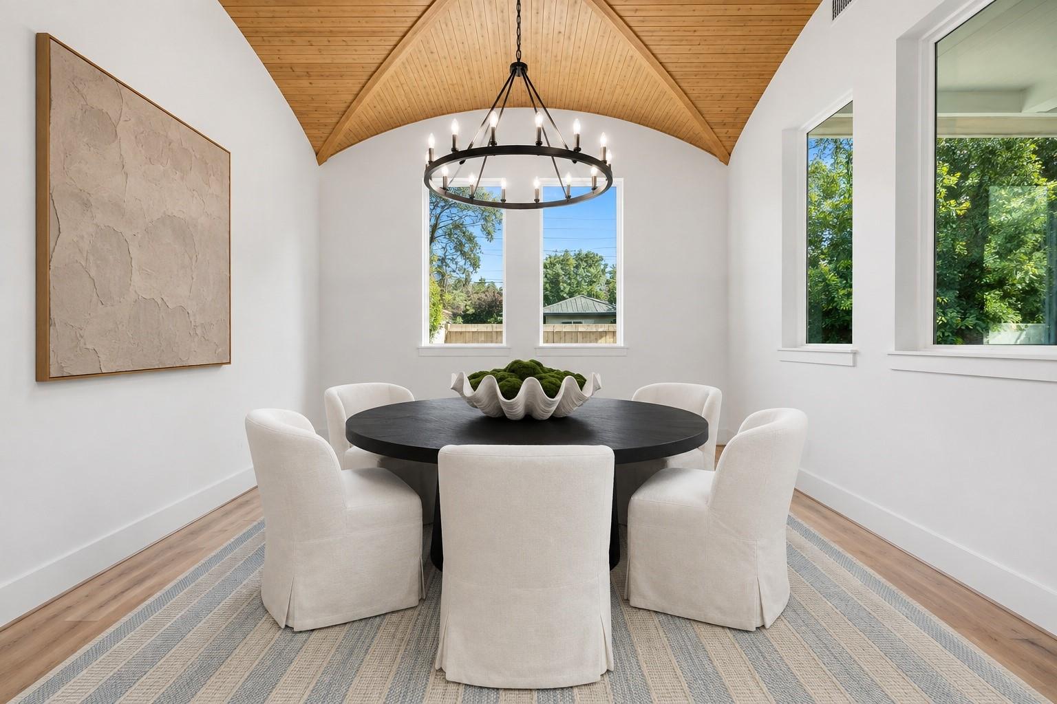 Dining room with a vaulted wood ceiling, round table, cream chairs, and circular chandelier.