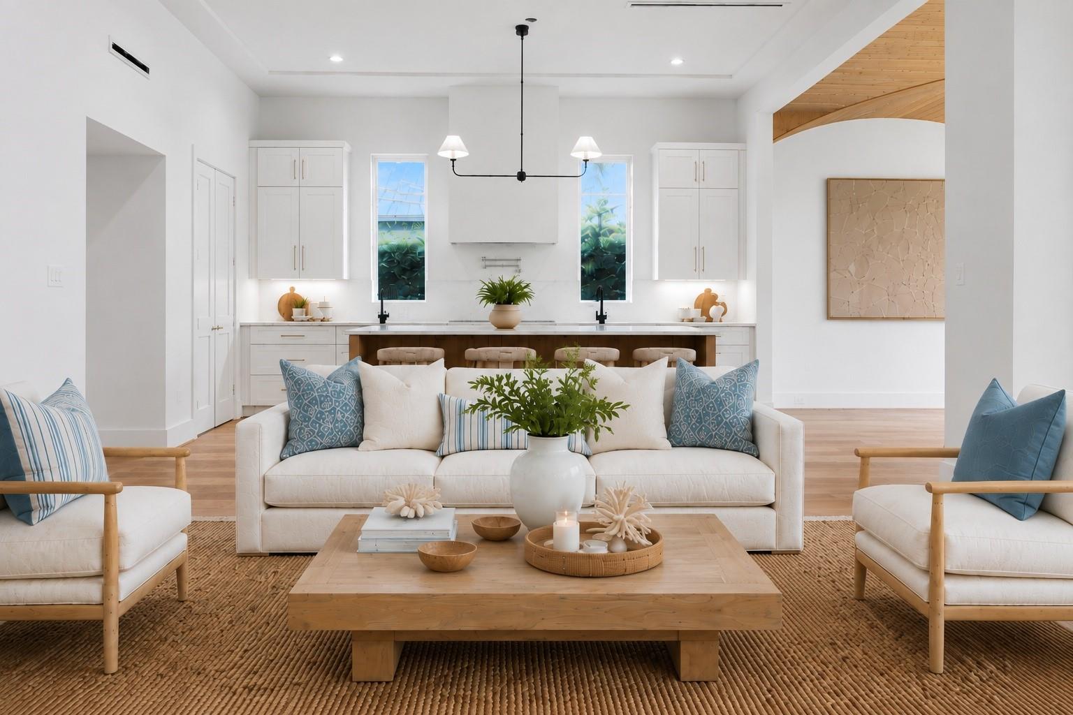 Staged living room with white seating, a large wood coffee table, and an open kitchen behind it.