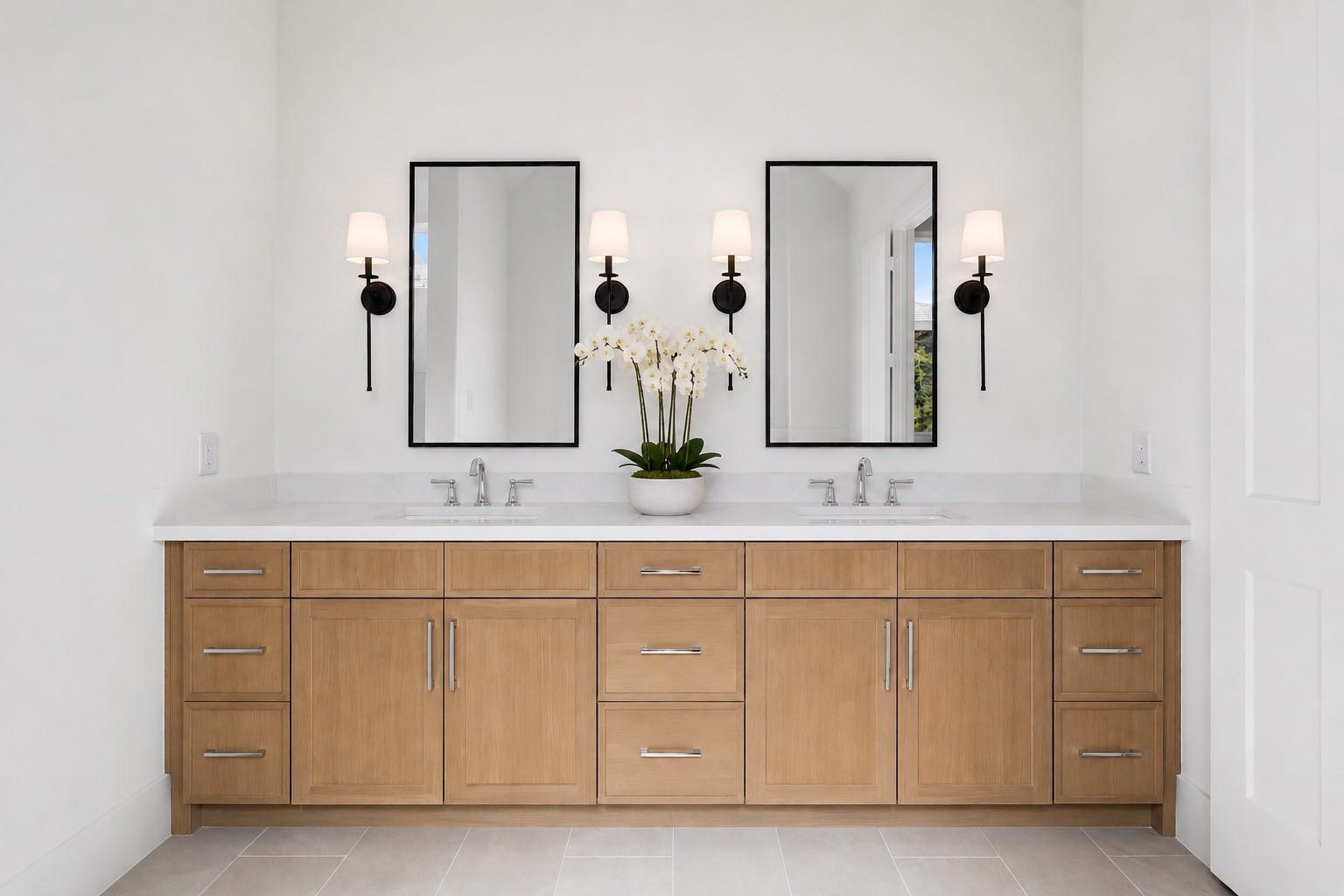 Bathroom with a light-wood double vanity, two sinks, black-framed mirrors, and a potted orchid.